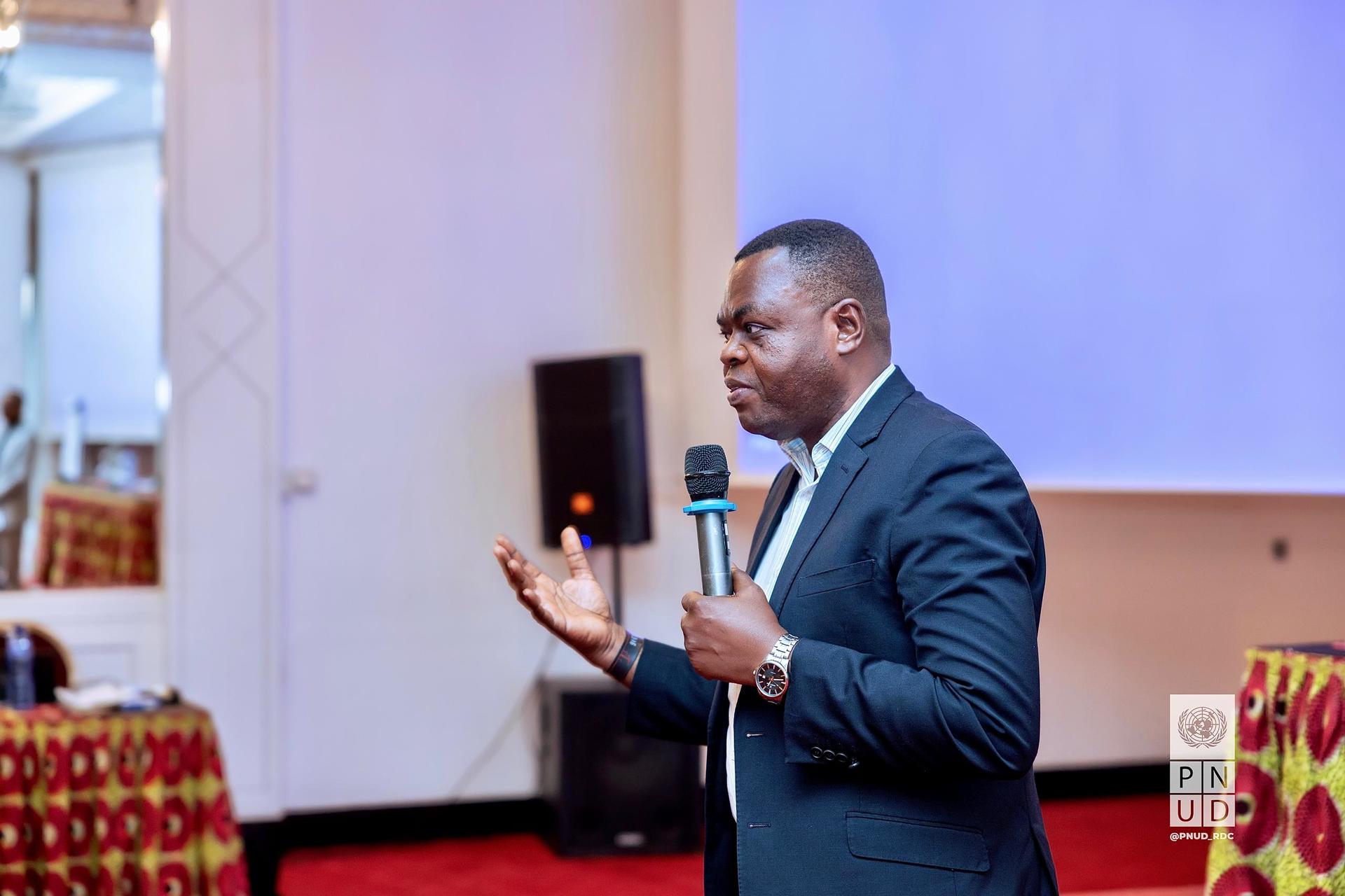 A man in a suit speaks passionately into a microphone at an event.