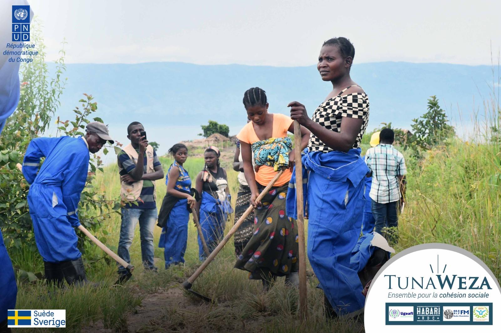 Group of people in blue overalls working in a field, with mountains in the background.