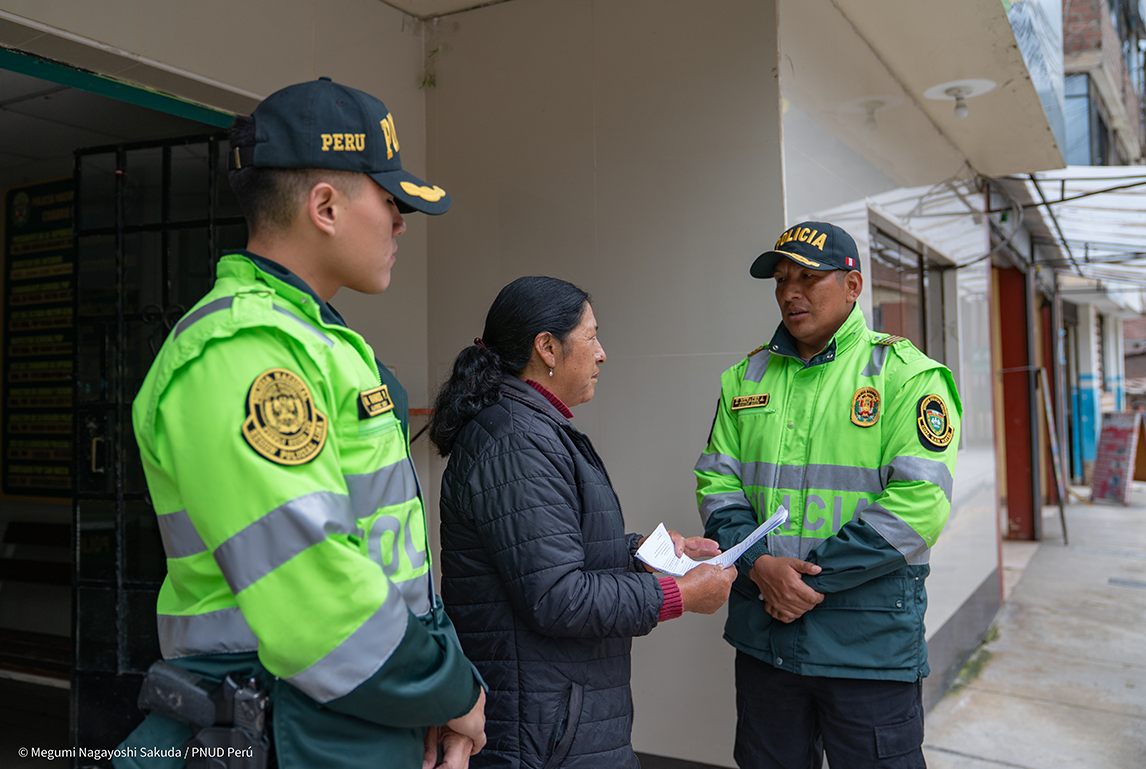 Two police officers in green uniforms are talking to a woman outside a building.
