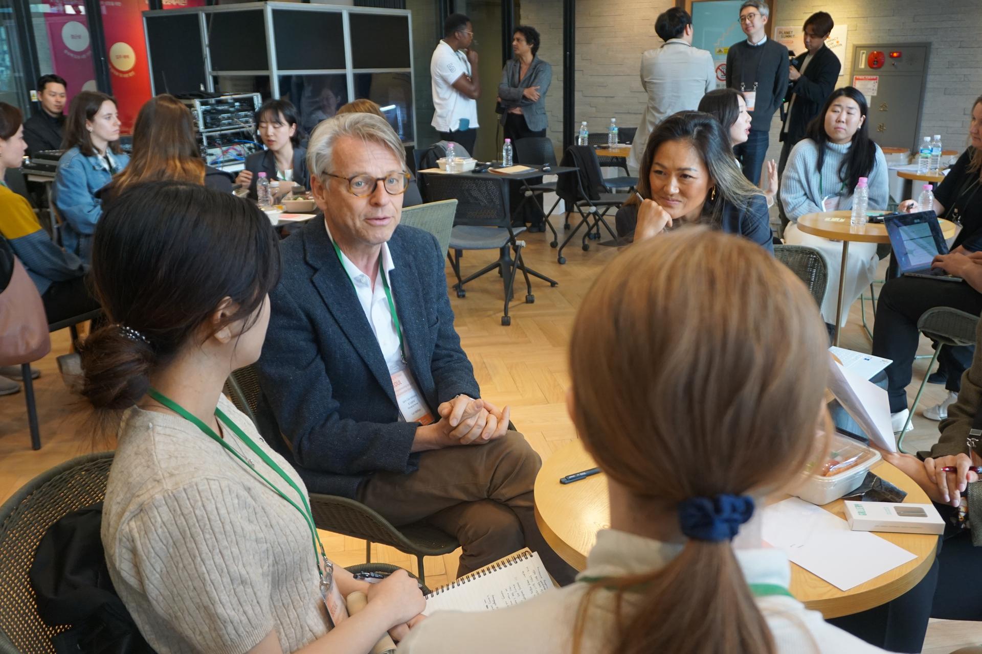 A group of people engaged in conversation at a round table in a bright, modern setting.