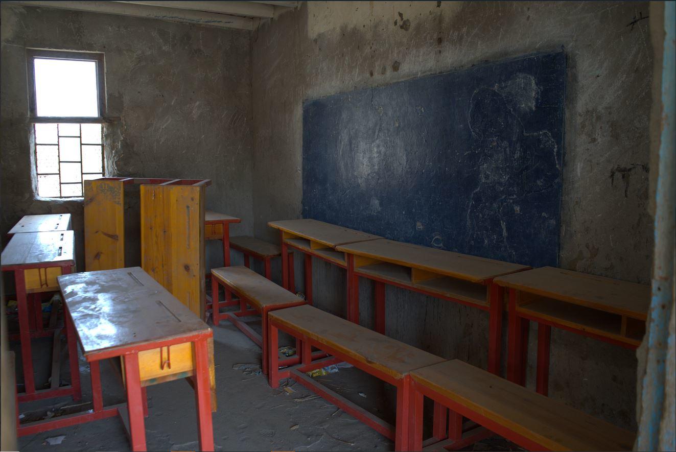Abandoned classroom with wooden benches and a worn blue chalkboard.