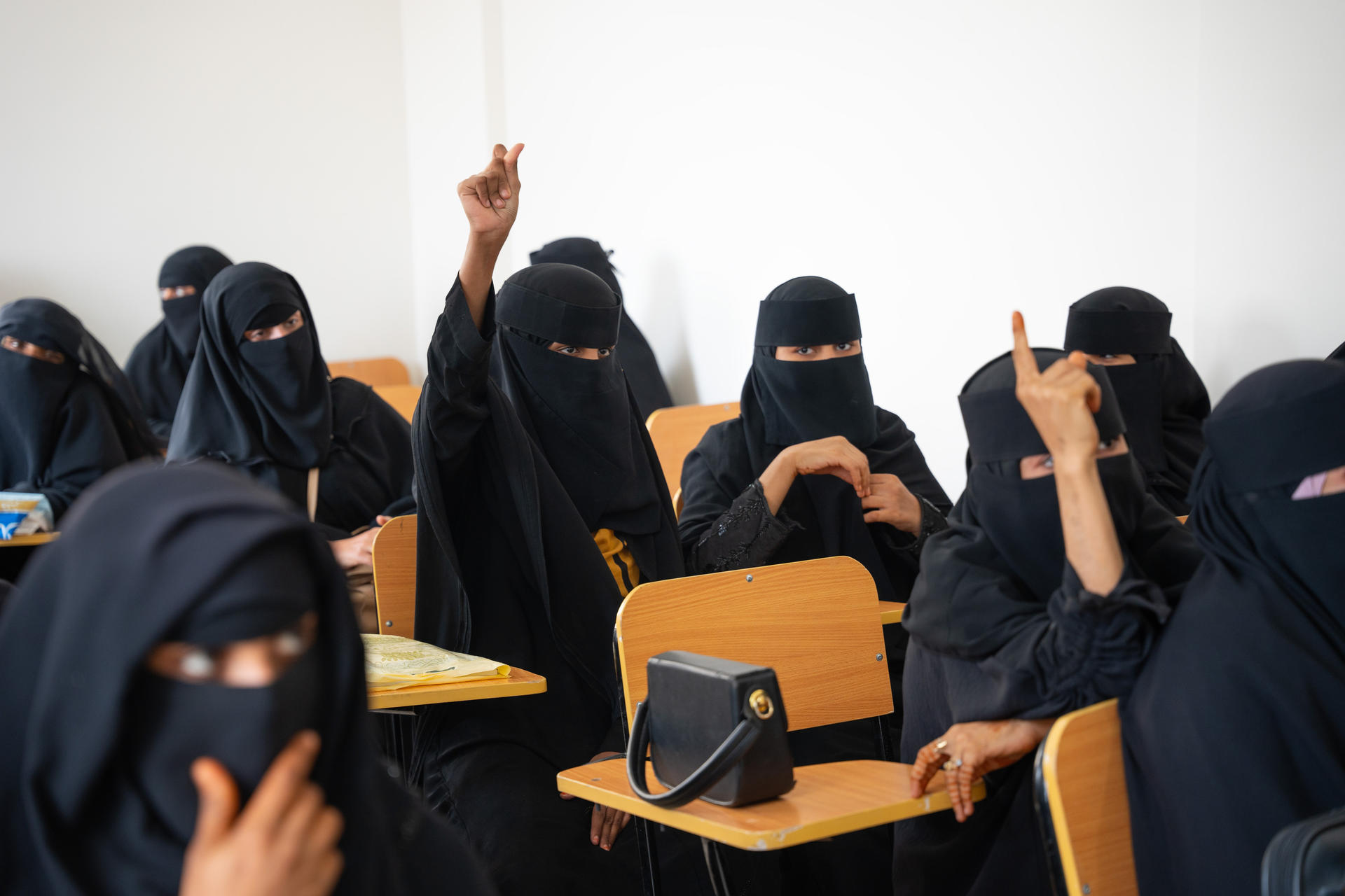 Students in black attire raise their hands in a classroom setting.