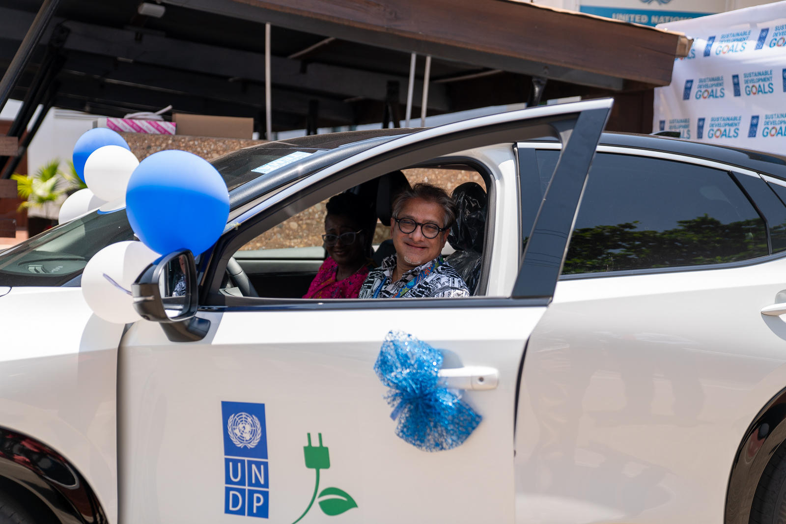 A child smiles while sitting in a decorated white car, balloons nearby.