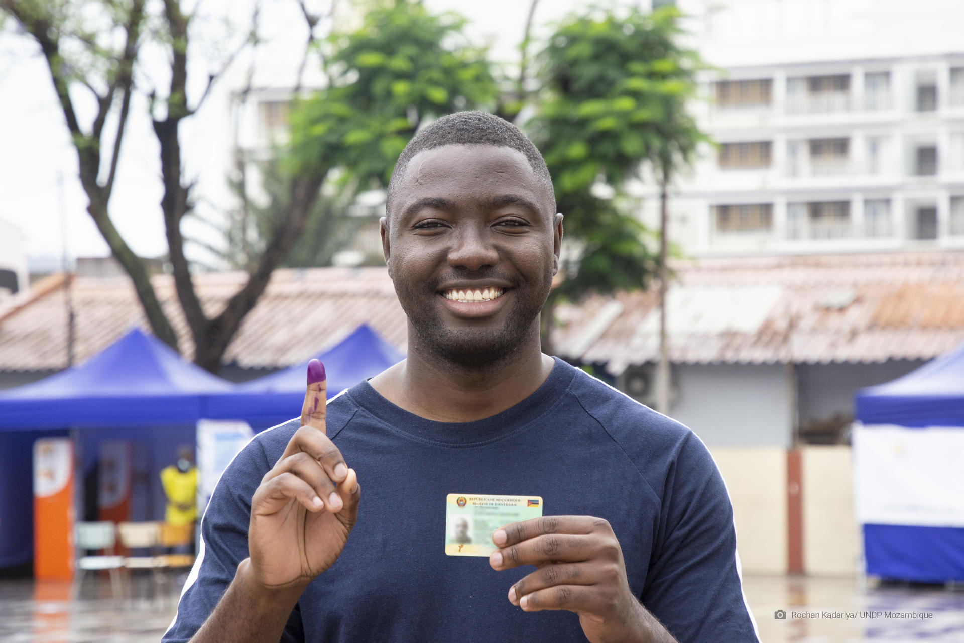 A man holding a voter ID card and showing an inked finger after voting