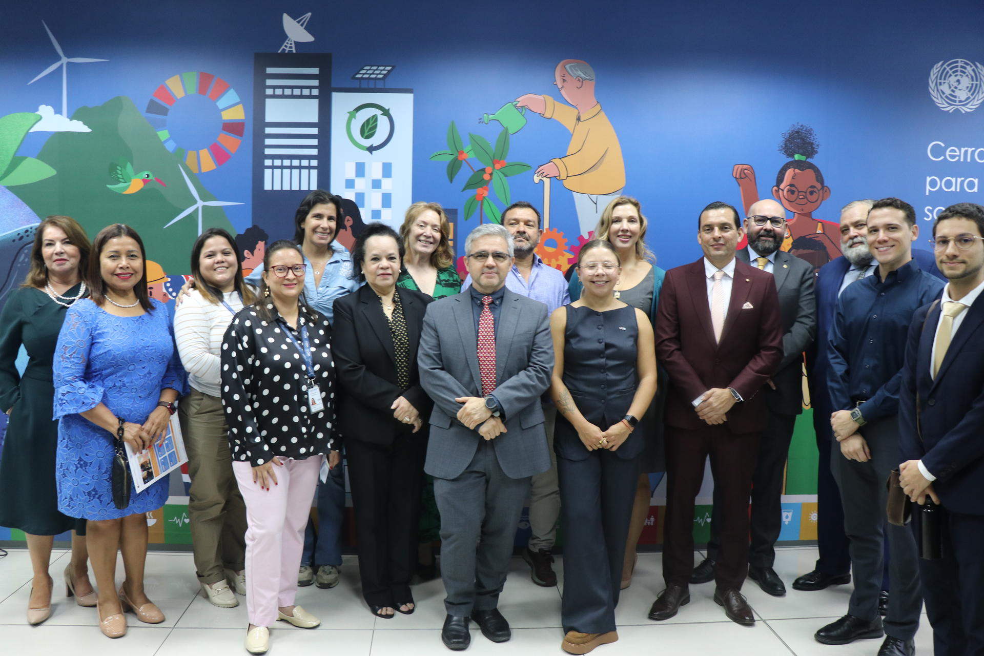 Group of diverse individuals posing together in an office, with a colorful mural in the background.