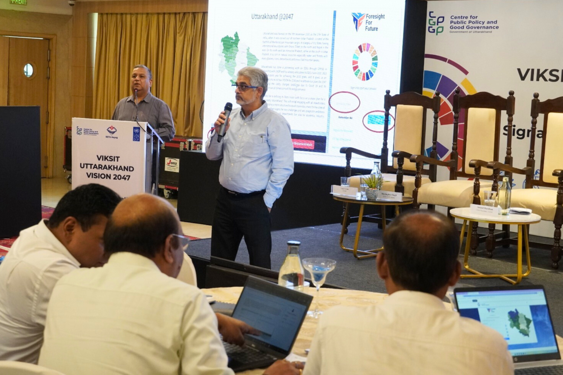 A speaker presenting at a conference, with an audience engaged at their laptops.