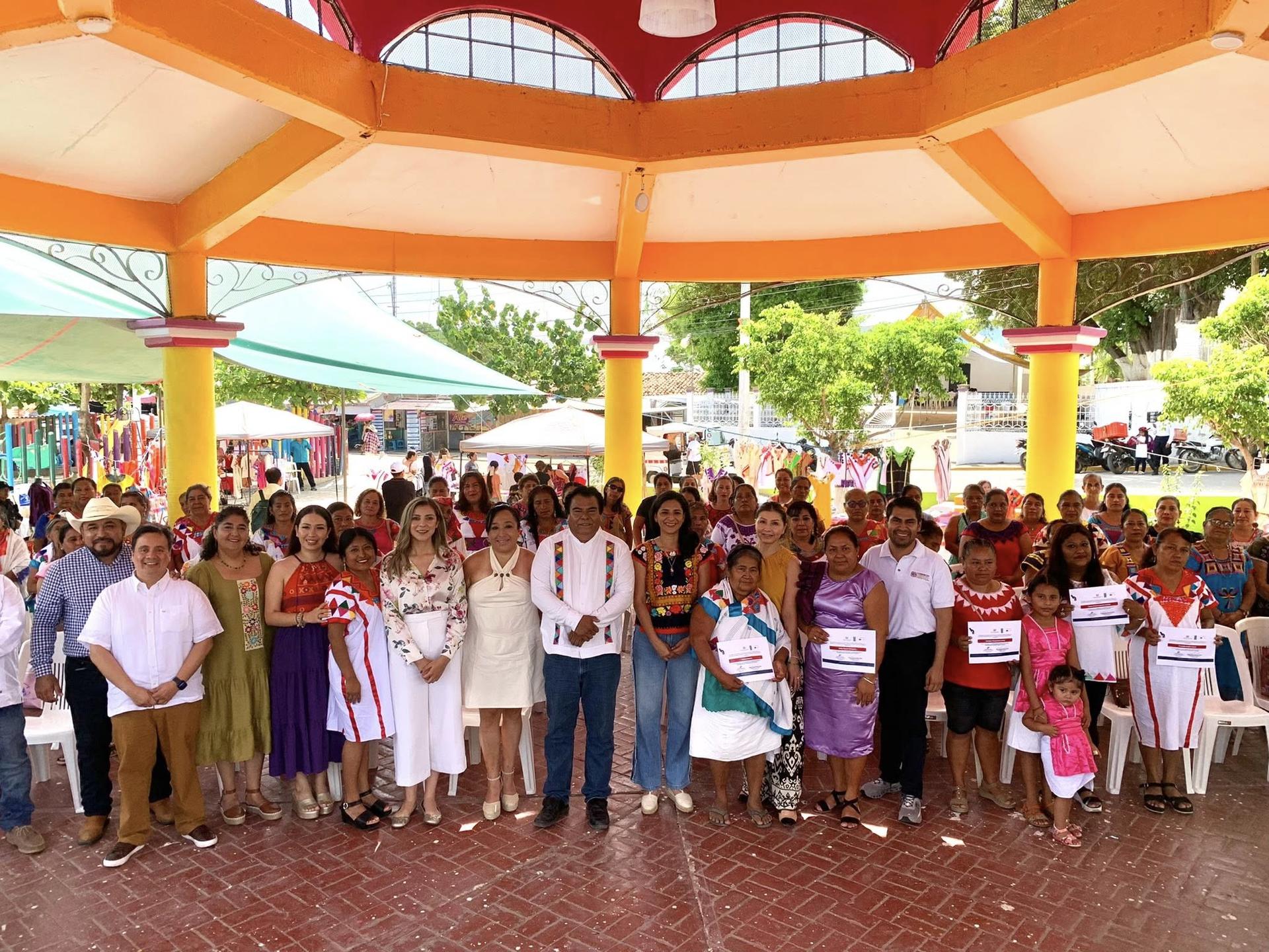 A large group of people gathered under a colorful gazebo in a festive outdoor setting.