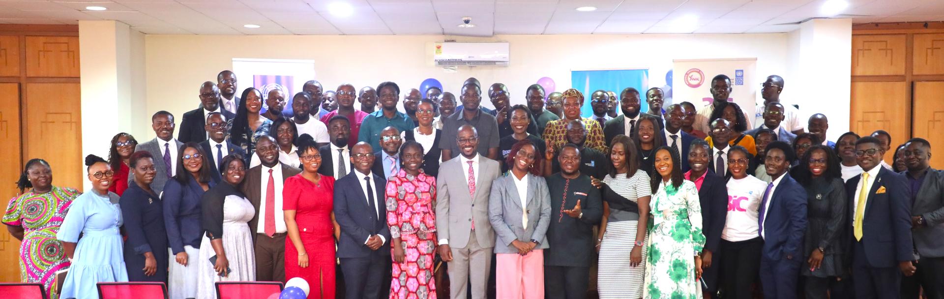 A large group photo of diverse individuals in formal and colorful attire, smiling together.