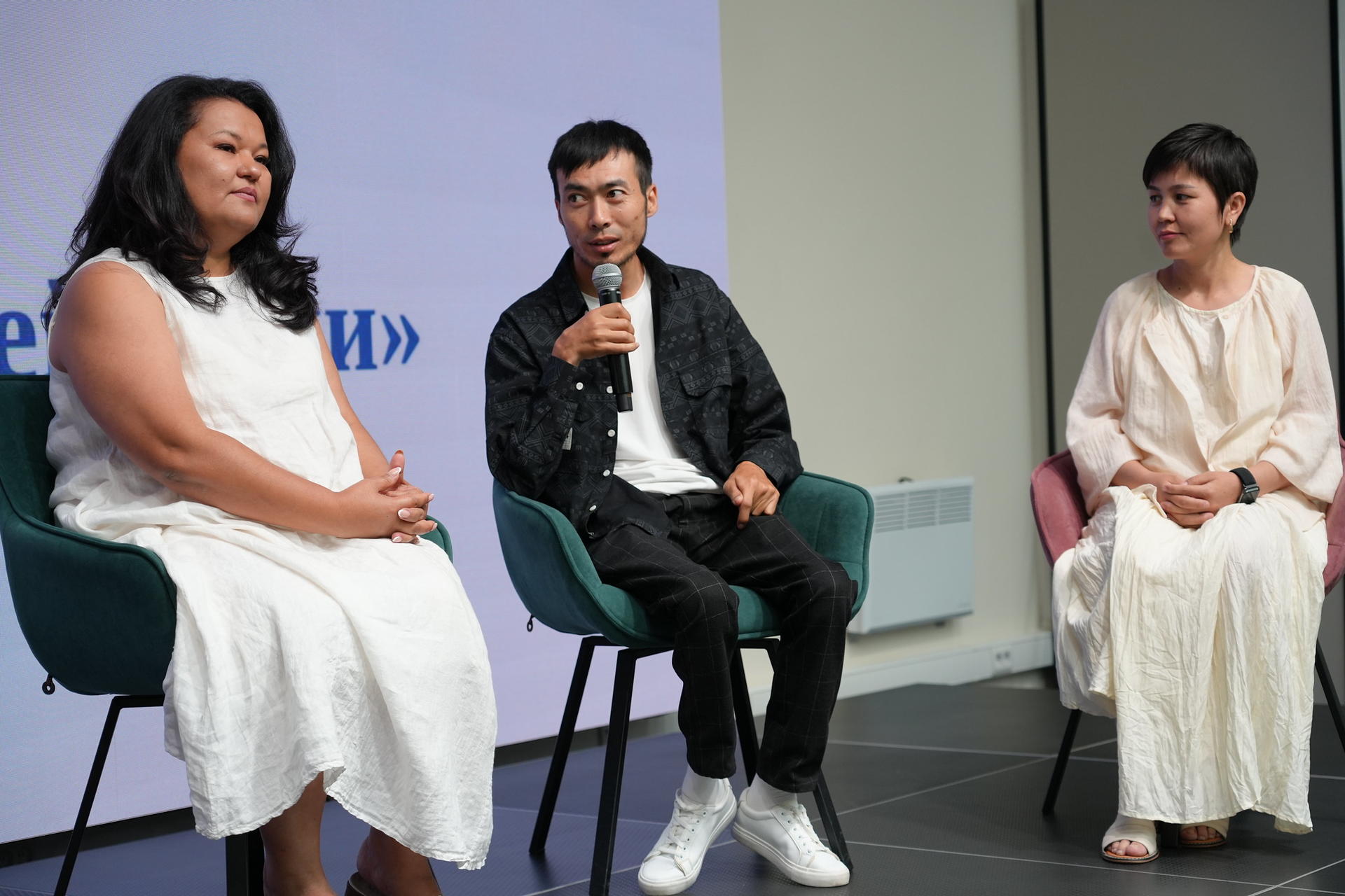 Three speakers sit on stage during a panel discussion, two women and one man.