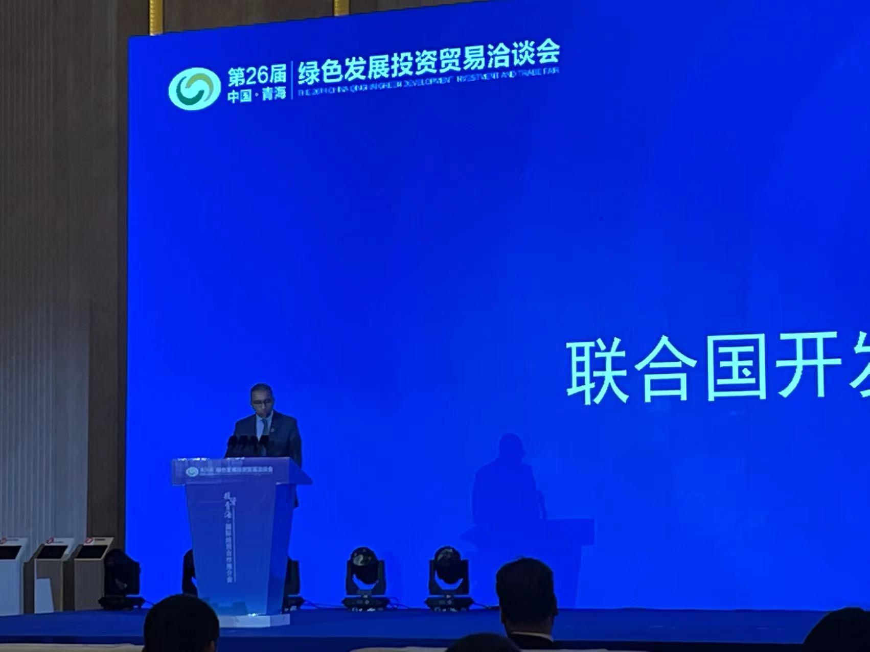 A man speaking at a podium against a blue backdrop during a conference.