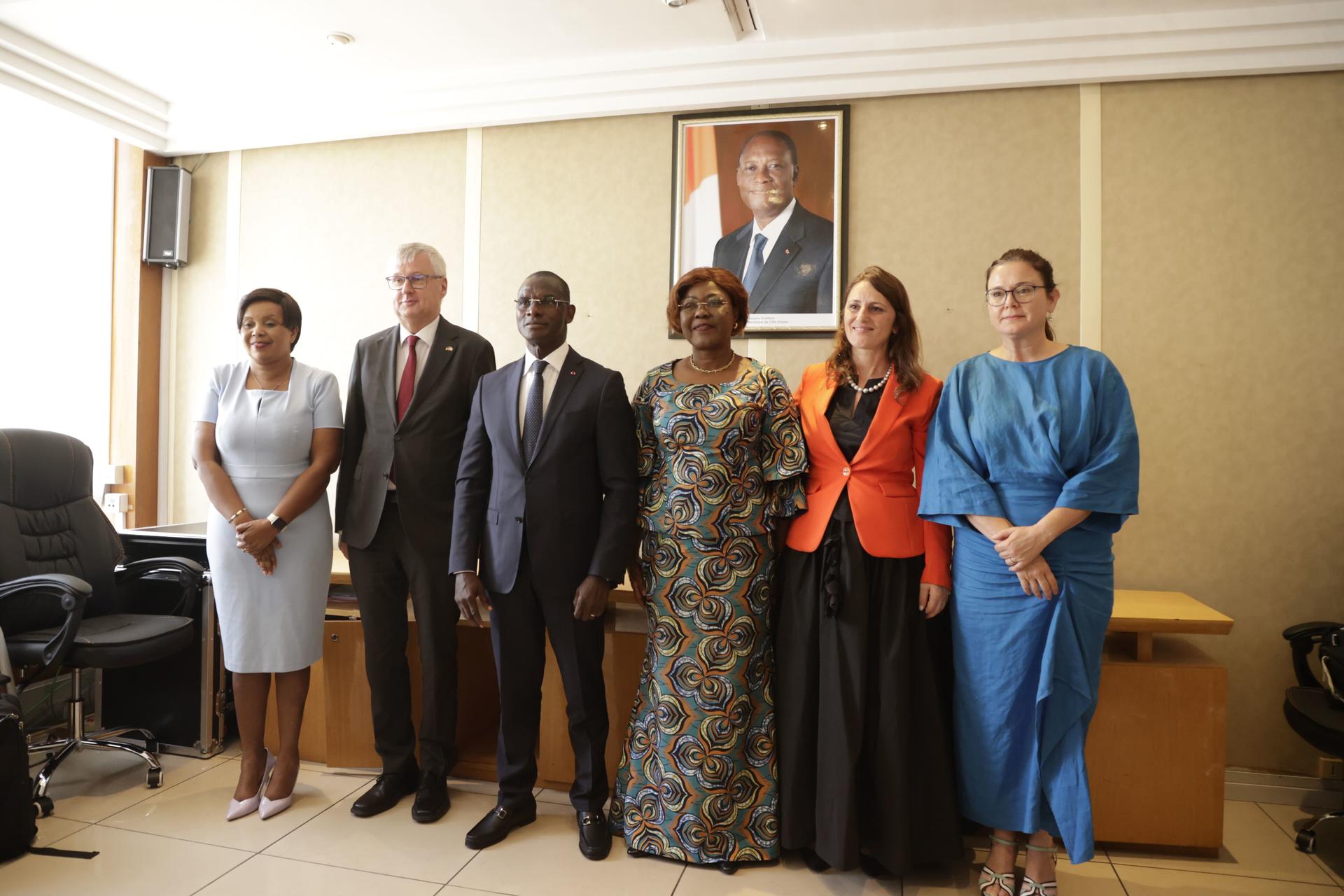 Six professionals standing in a formal setting, with a portrait in the background.
