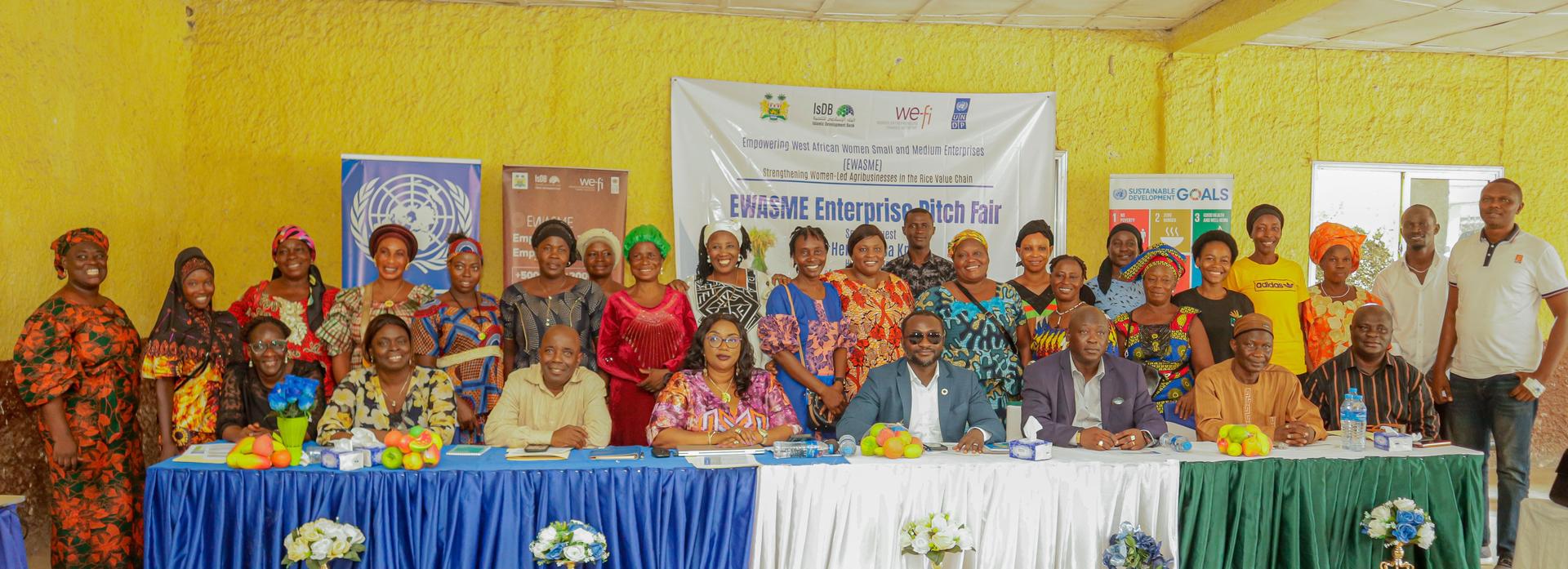 Group photo of a diverse audience seated and standing in a brightly lit room with colorful attire.