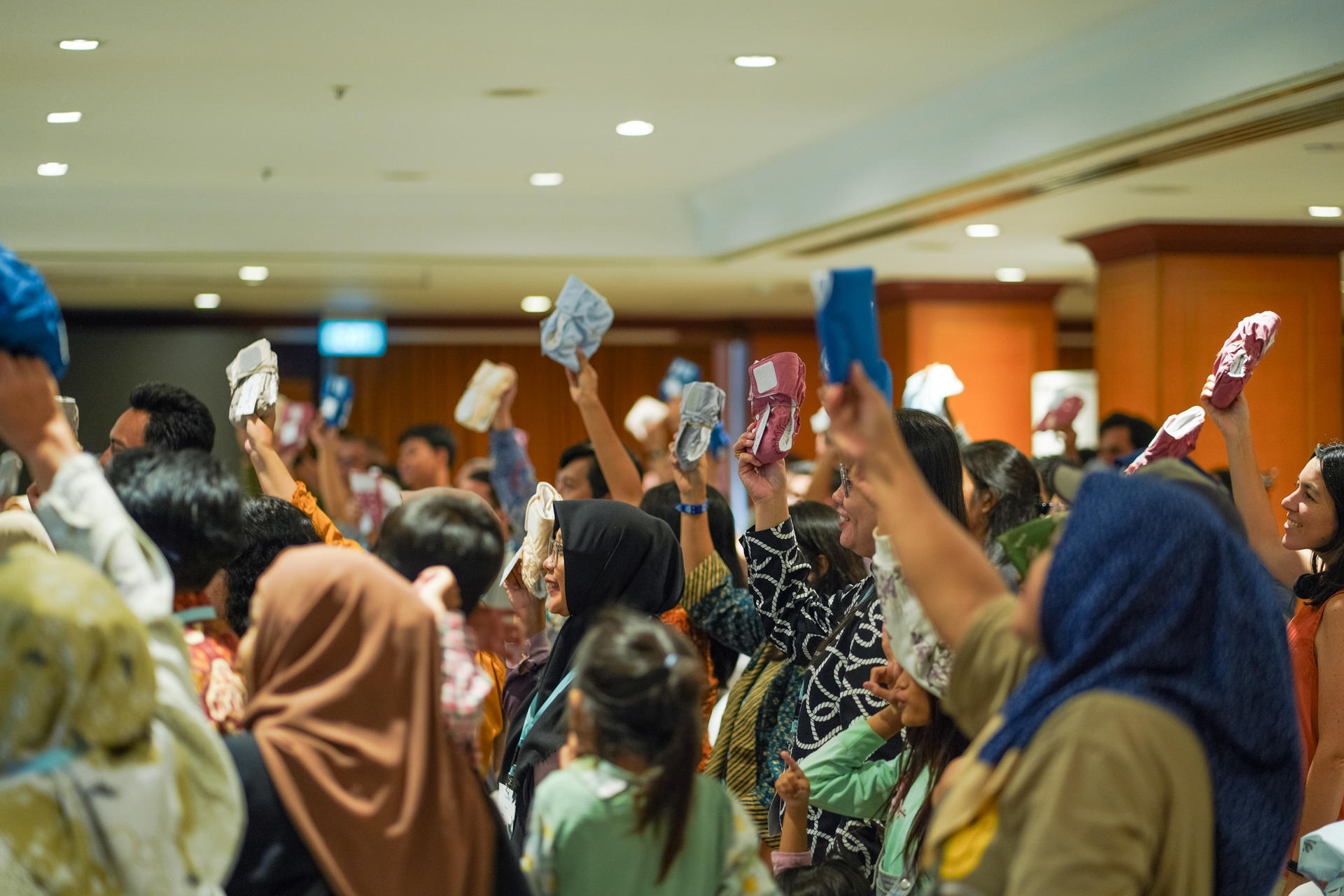A crowd of people in a spacious indoor setting raising colorful fabric pieces.