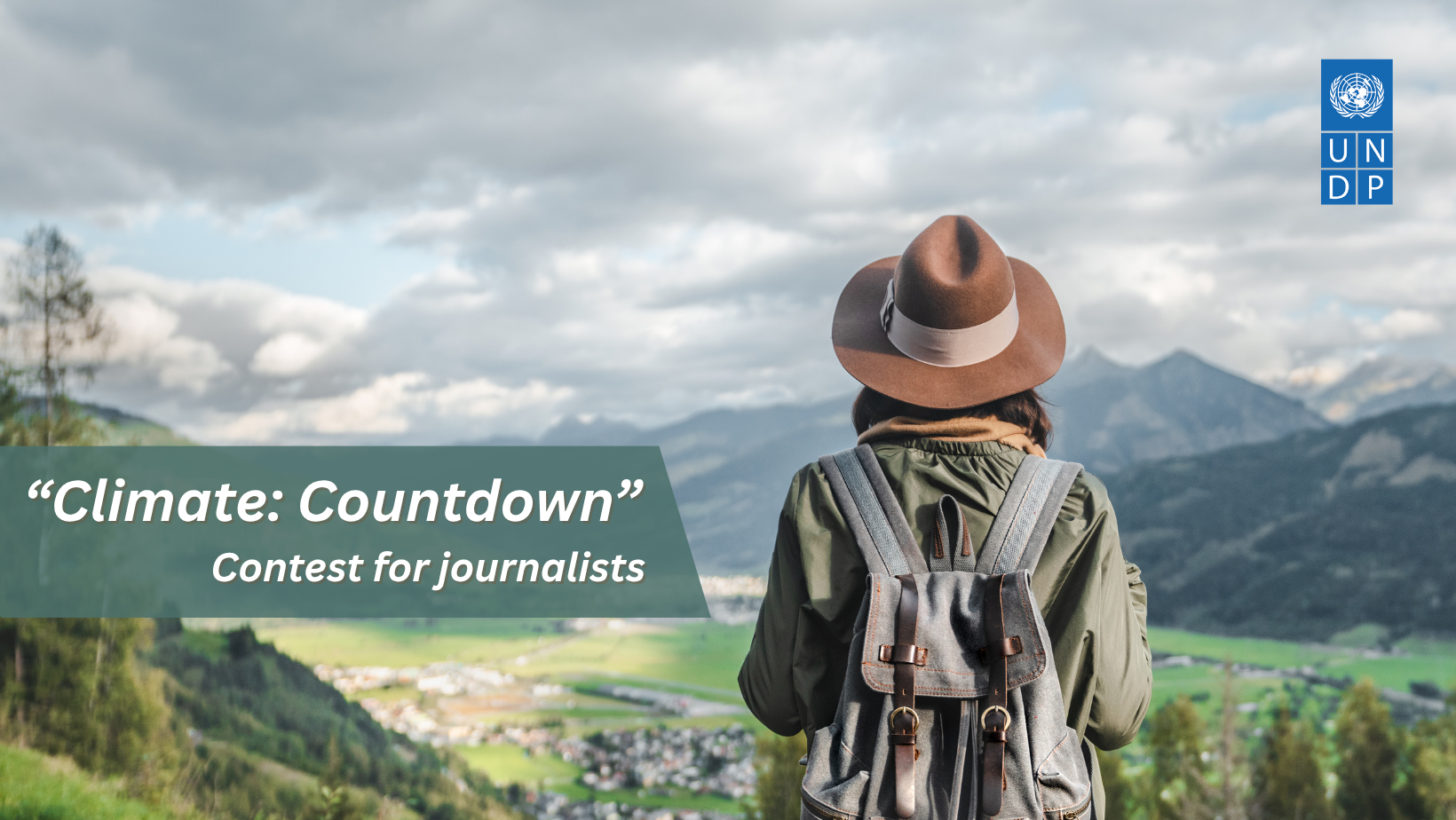 Person in a hat and backpack looking at a scenic mountain landscape with clouds.