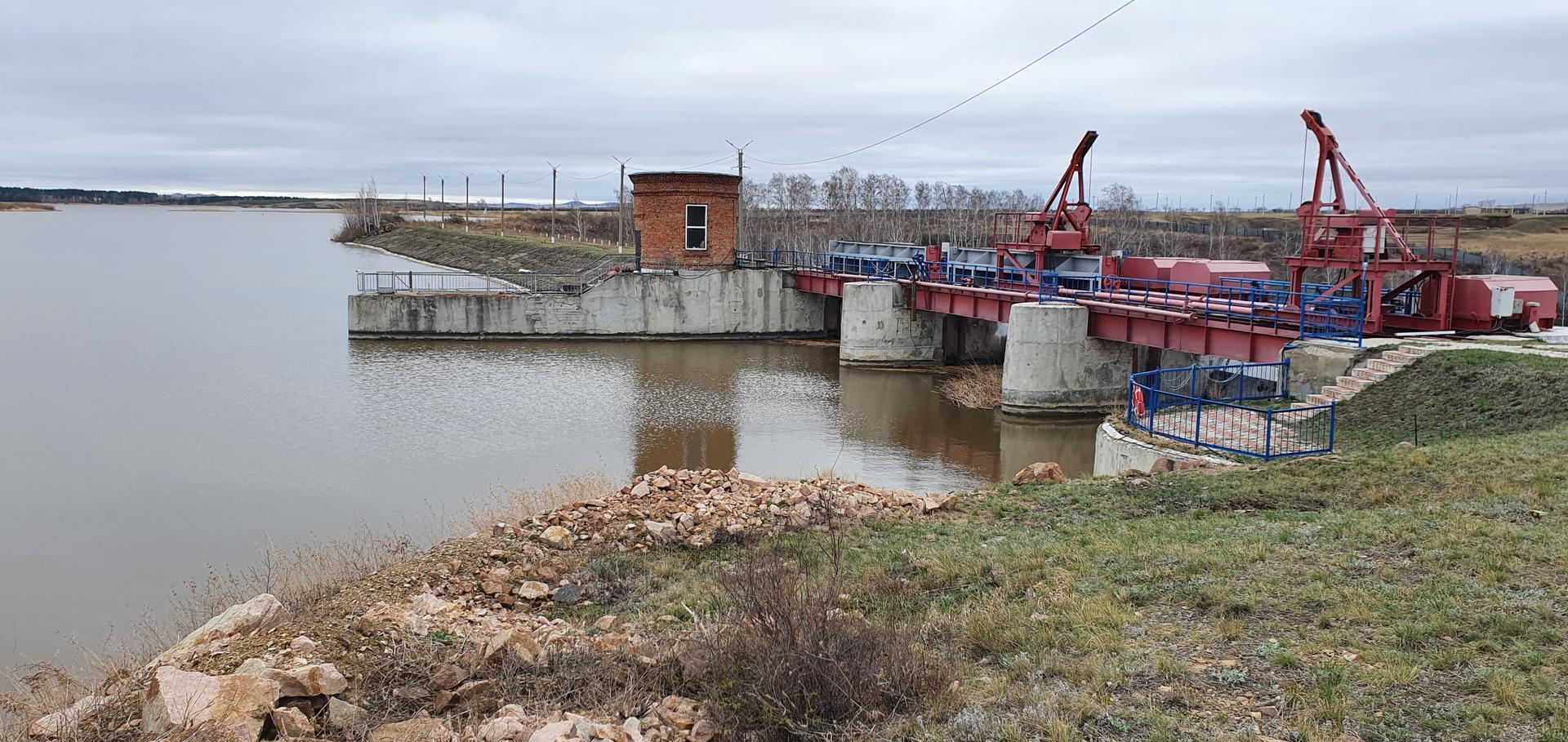 A hydraulic structure on a riverbank with red machinery and cloudy skies.