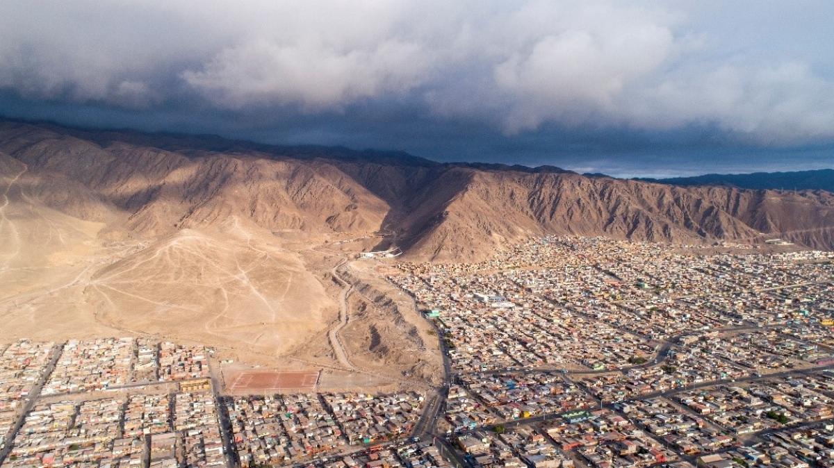 Aerial view of a city surrounded by mountains under a cloudy sky.