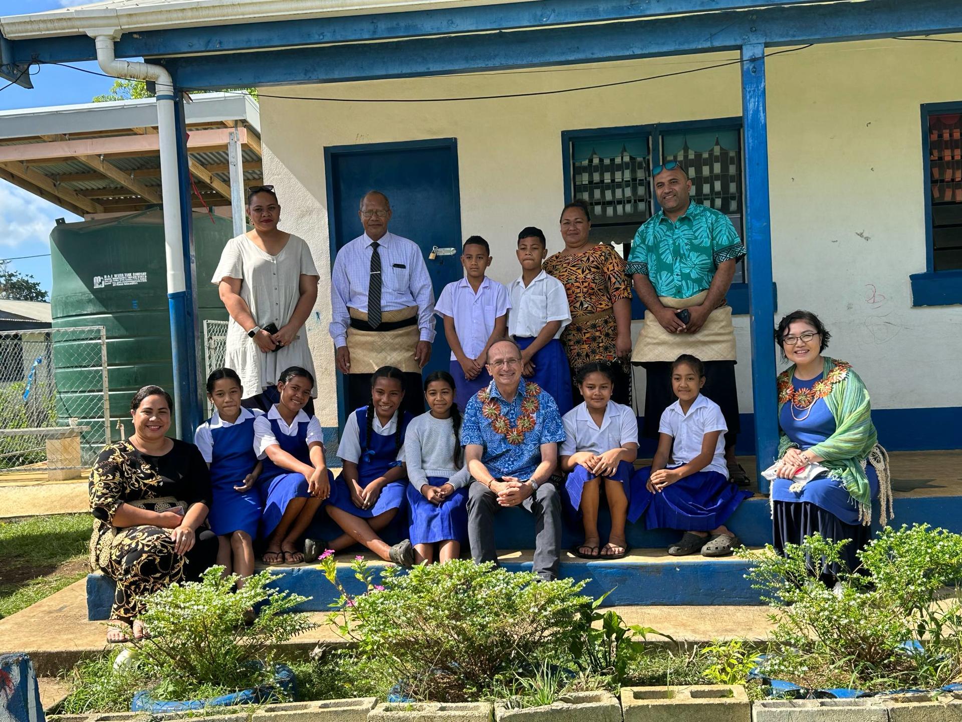 Group of students and adults posing outside a school building with blue accents.