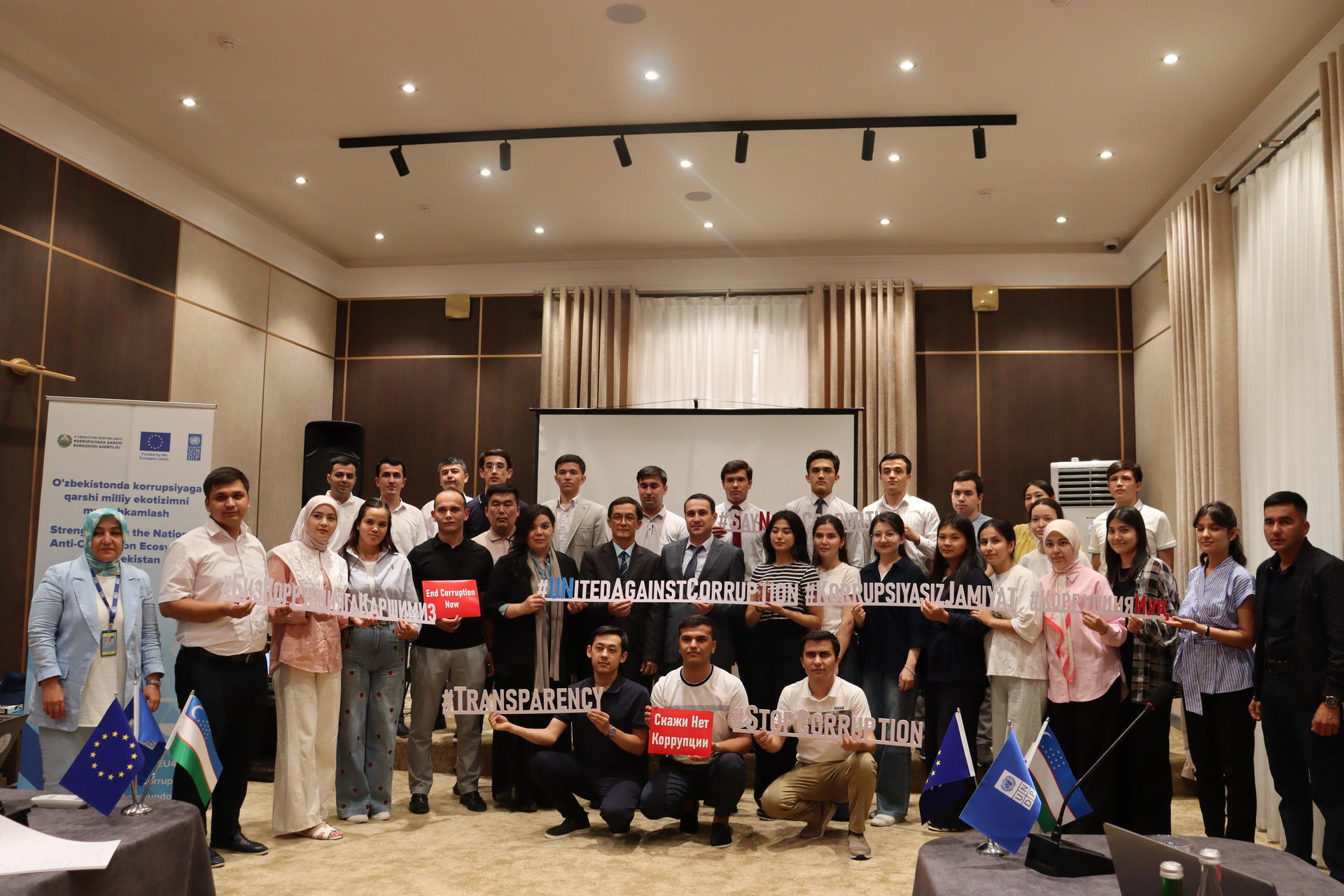Group photo of diverse participants in a conference room, holding various signs and flags.