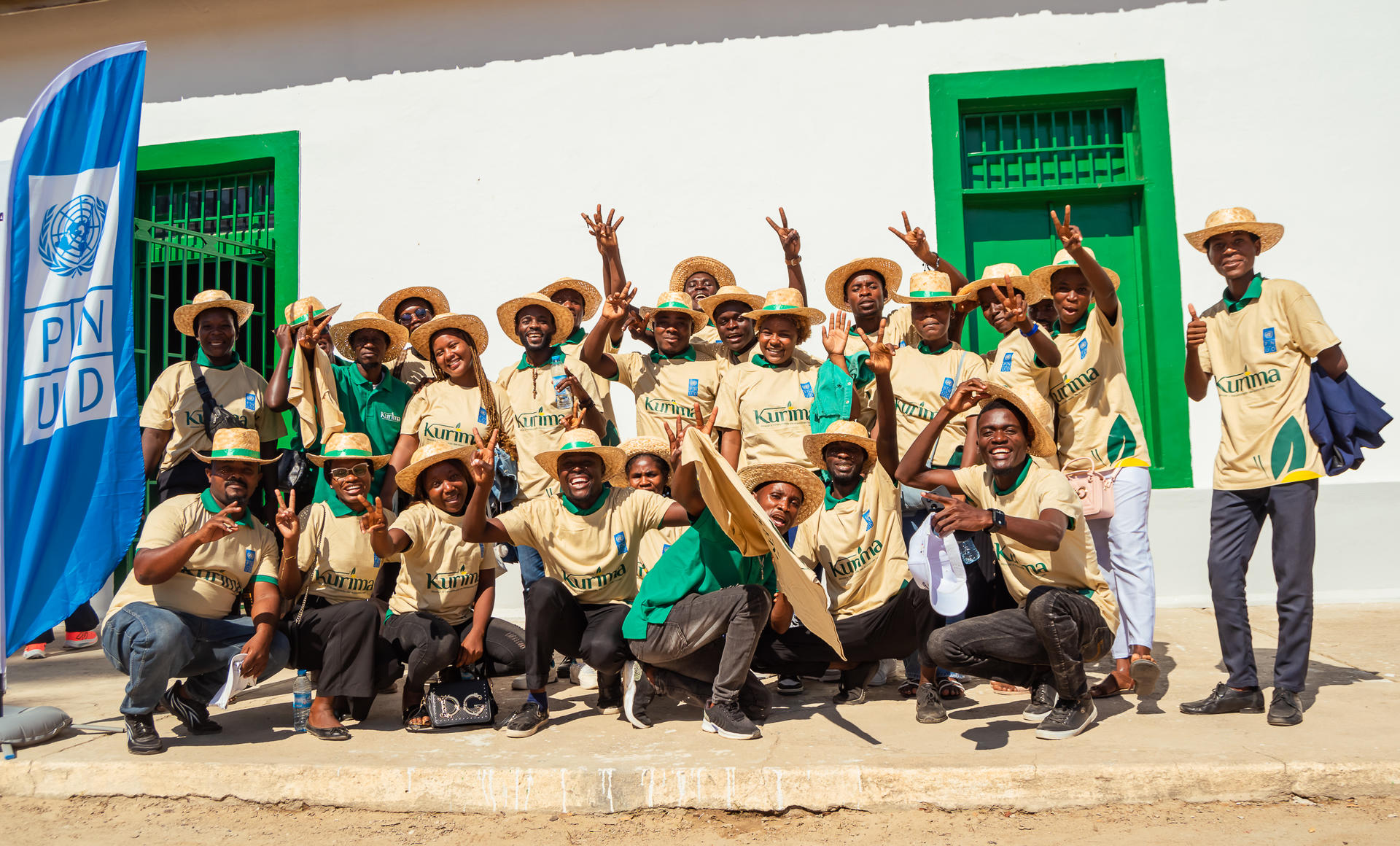 A group of people wearing matching shirts and hats poses joyfully outdoors near a building.