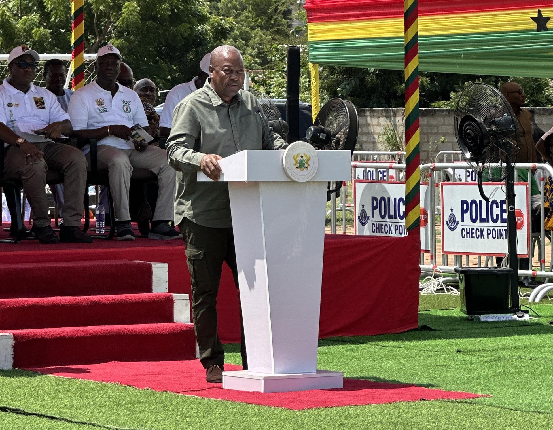A man in a military uniform speaks at a podium surrounded by seated officials at an outdoor event.