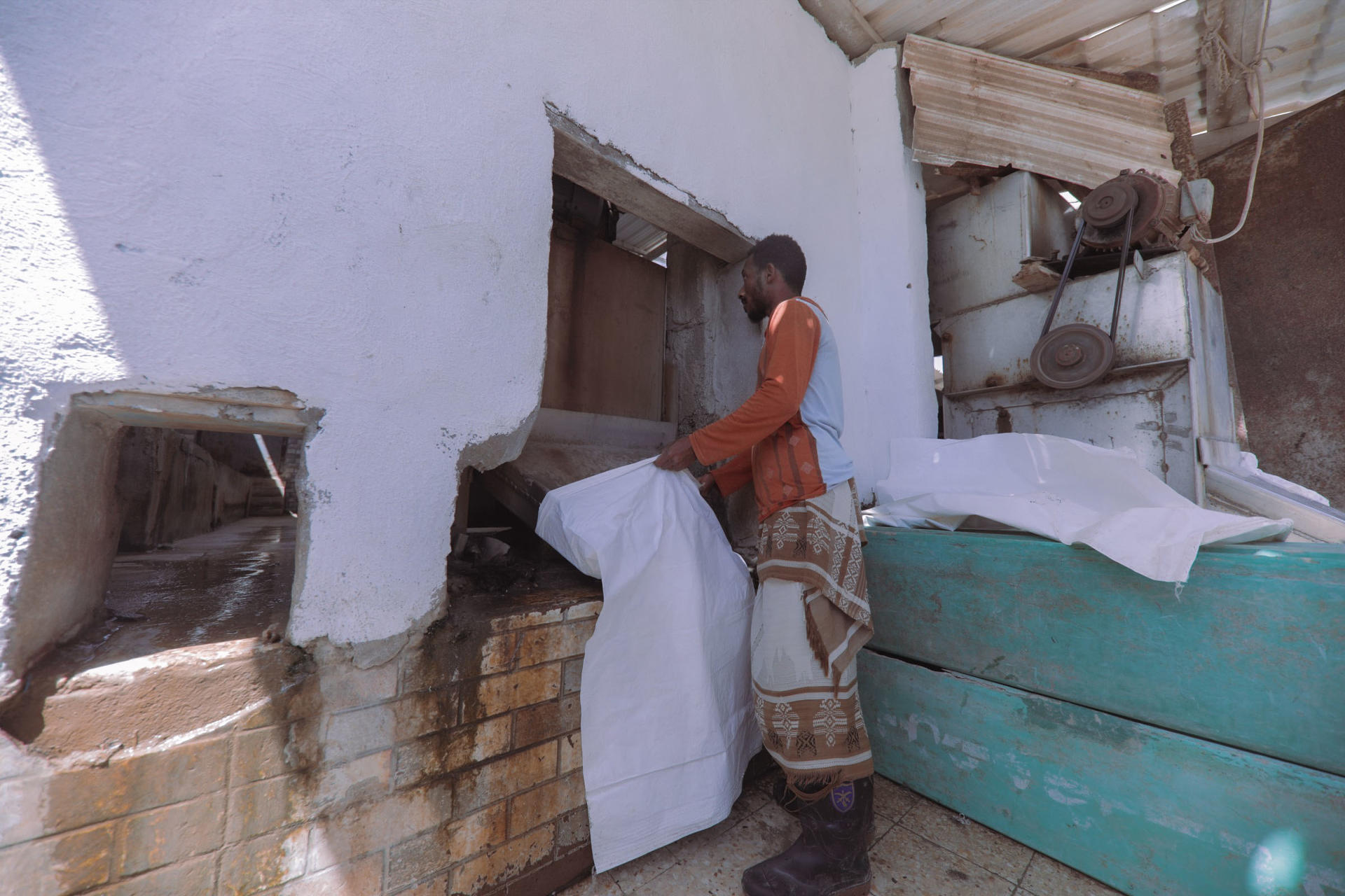 A person in a brown shirt covers a damaged wall with white fabric inside a room.