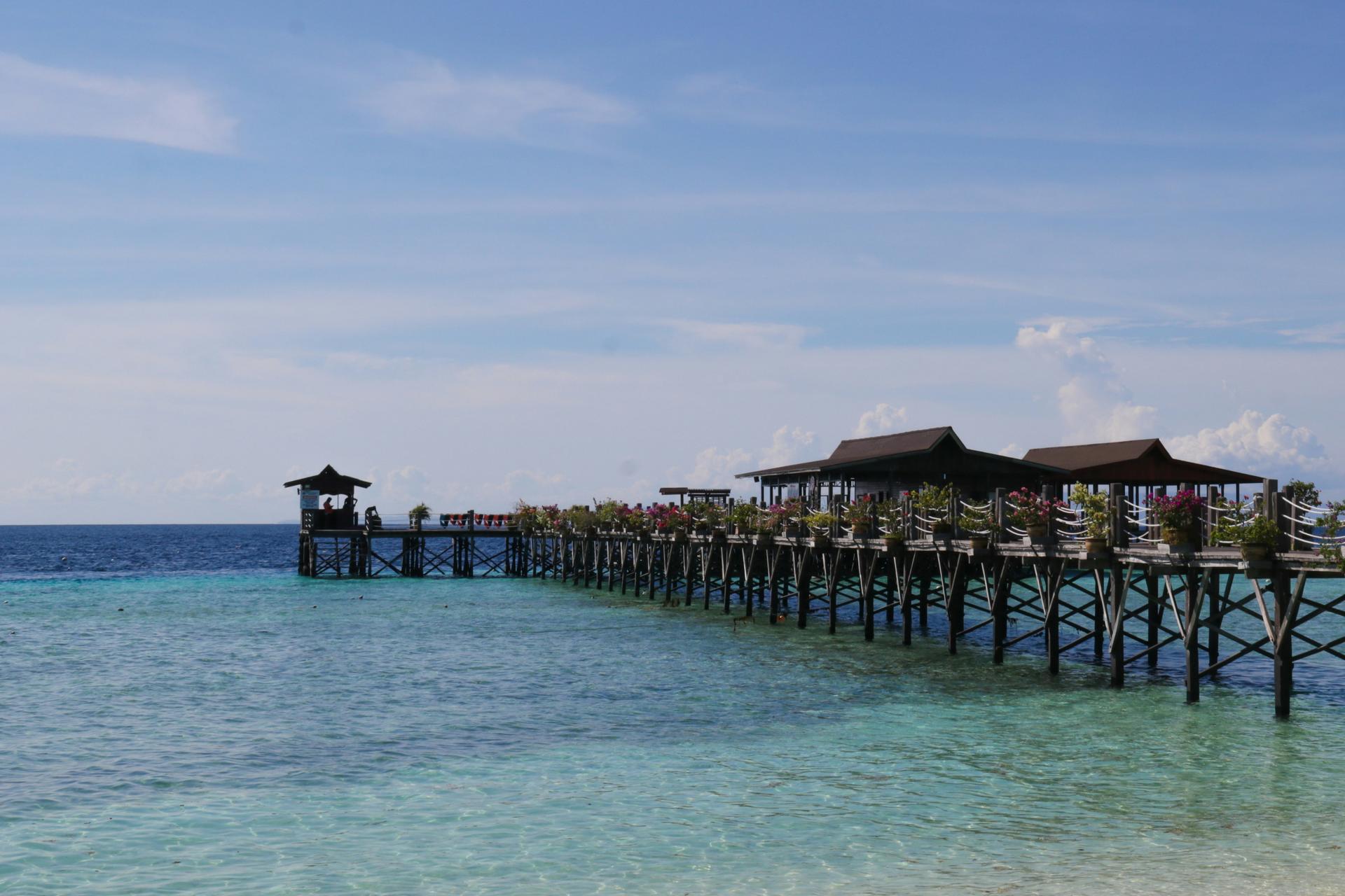 Wooden pier extending over clear blue water under a bright sky.