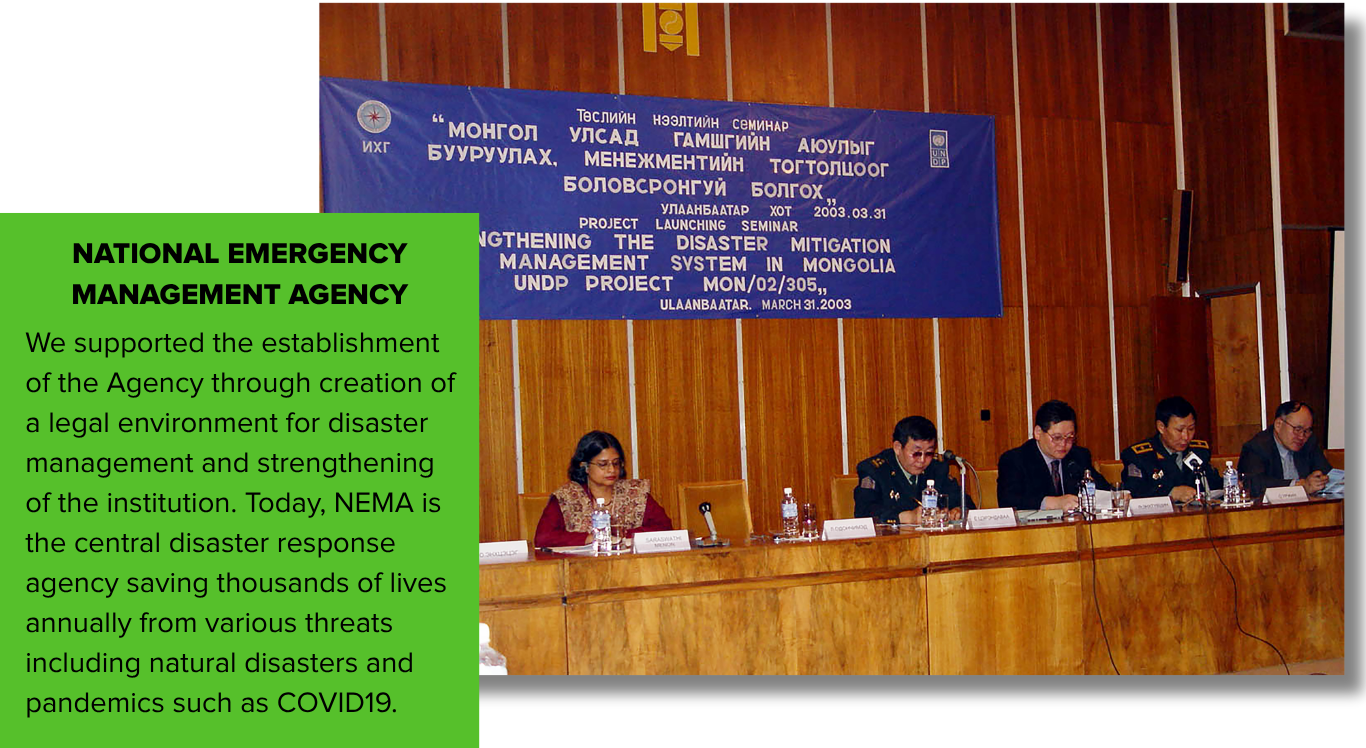 Panel discussion with officials seated at a table in front of a blue banner and green text box.
