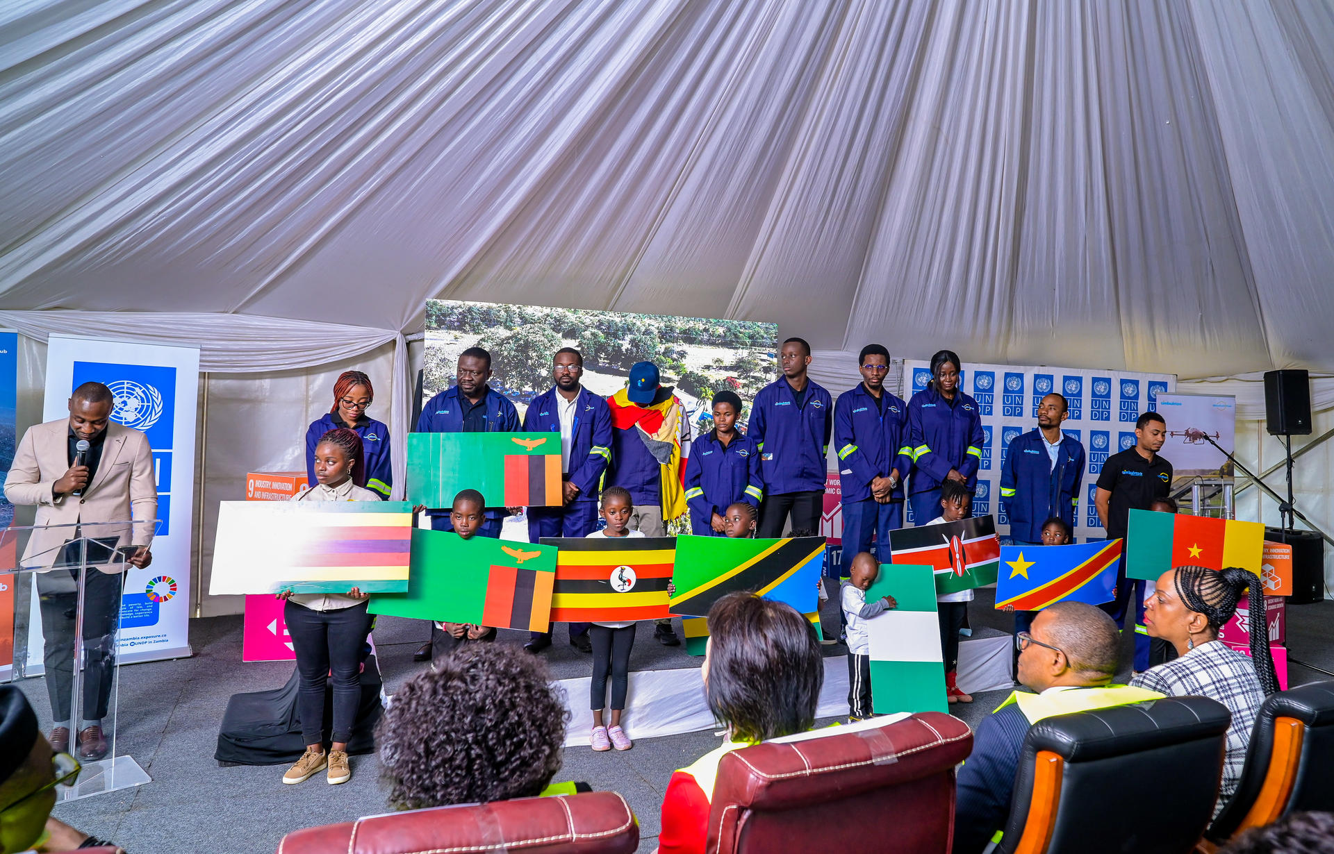 A group of people in dark blue MineTech mining jackets holding flags, standing inside a large tent.
