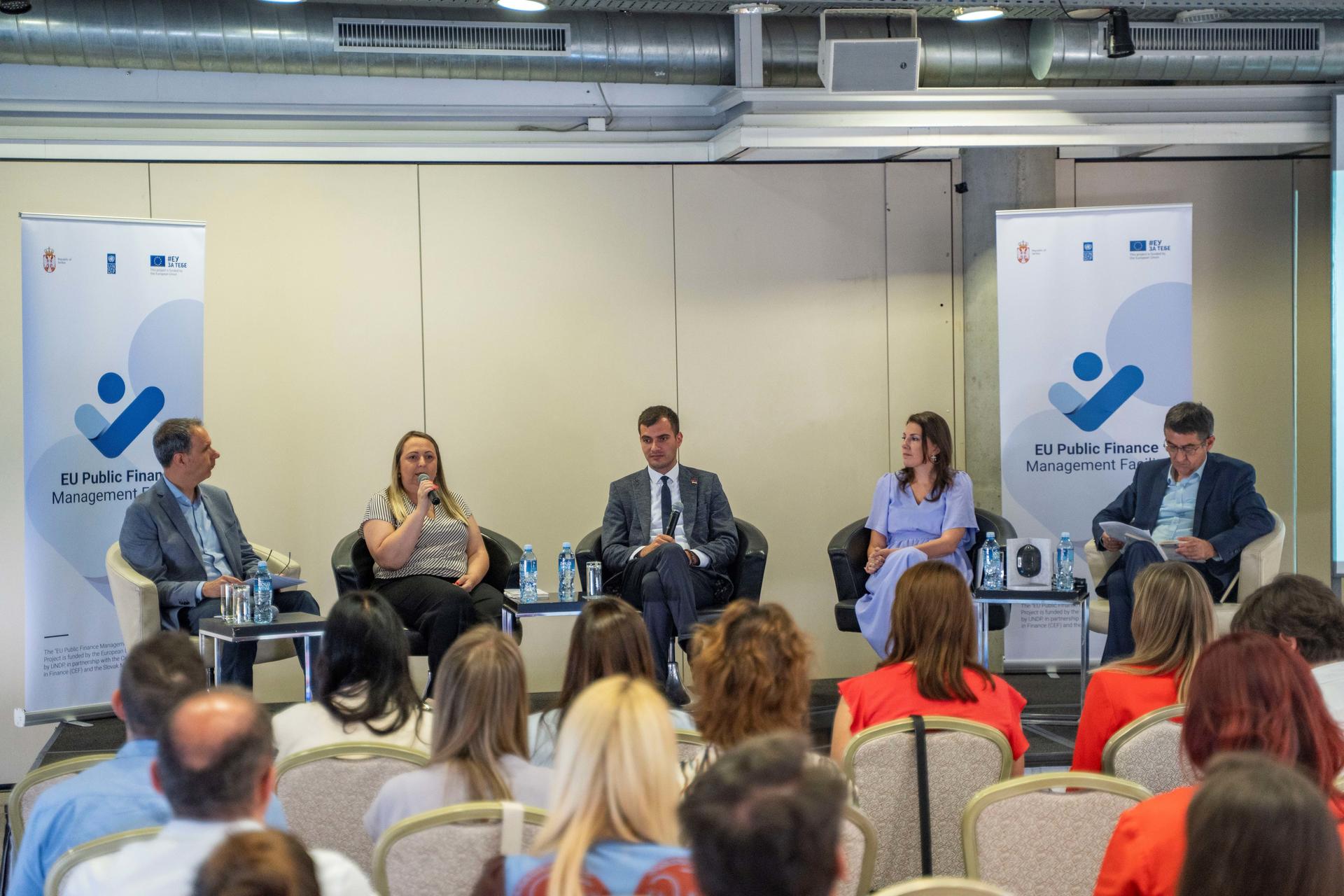 Panel discussion featuring five speakers at a formal event, seated in front of an audience.