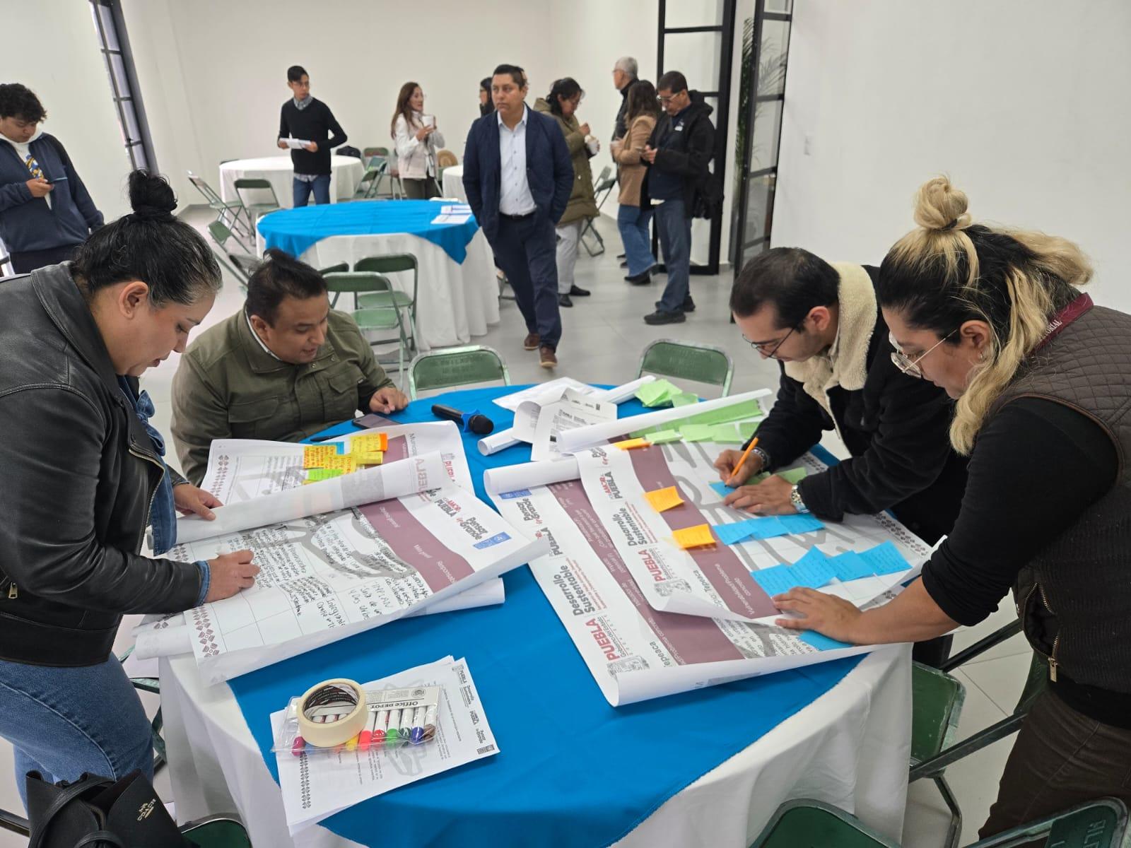 Participants collaborate on large plans at a workshop, using sticky notes and discussing details.