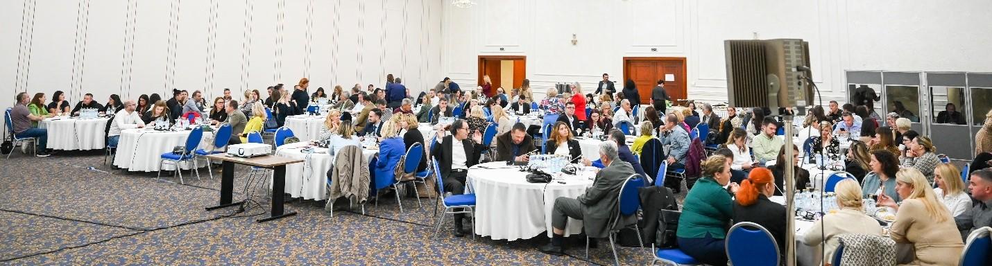 A large group of people seated at round tables in a well-lit conference hall.