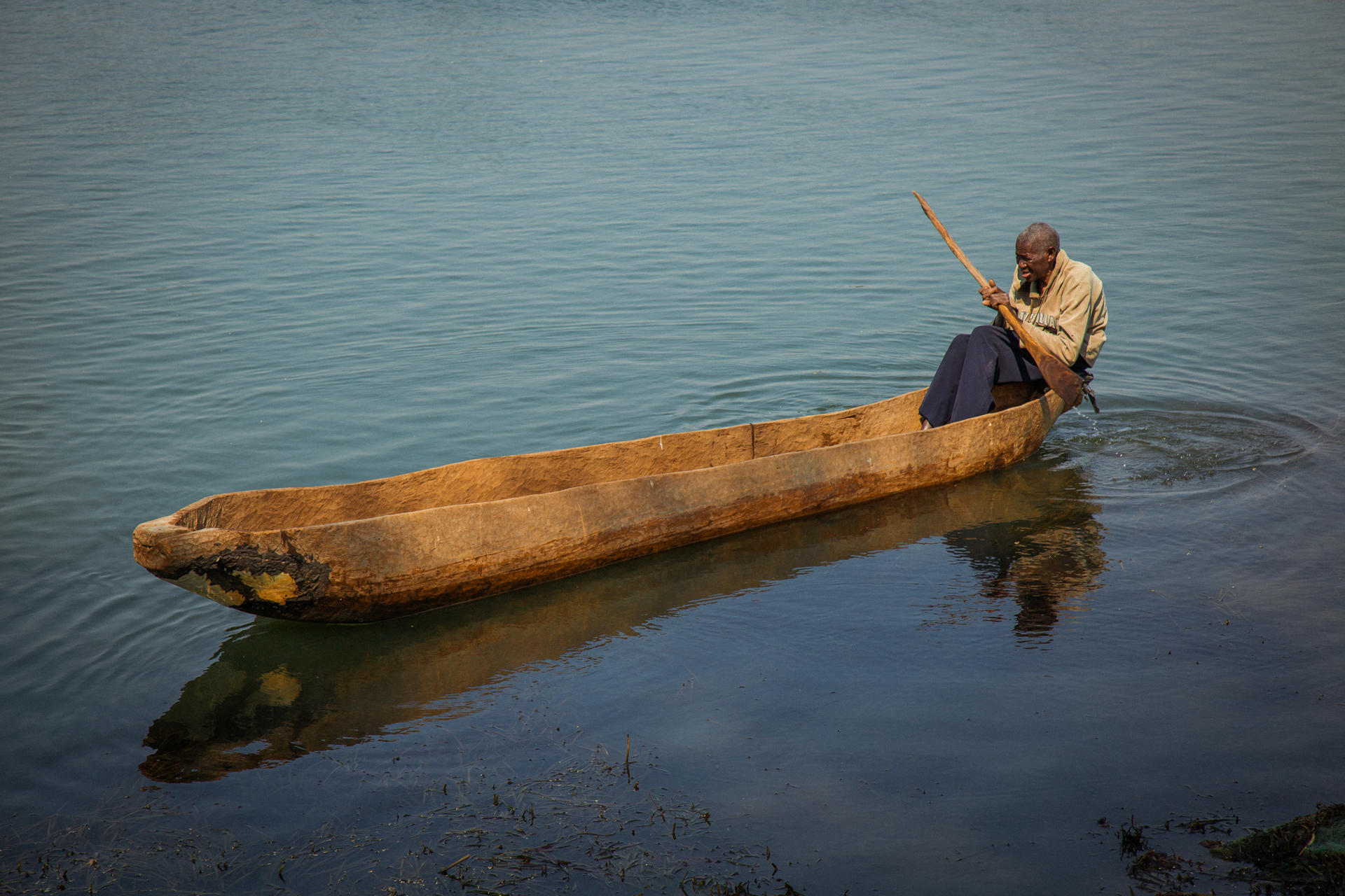 A Zambian rowing a narrow, canoe on calm water.