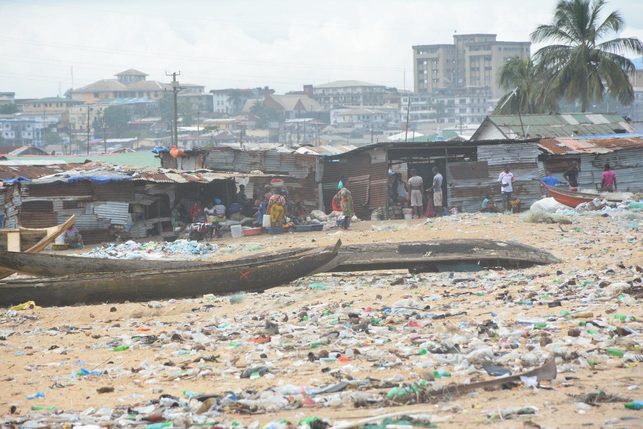 A cluttered beach strewn with garbage and makeshift huts in the background.