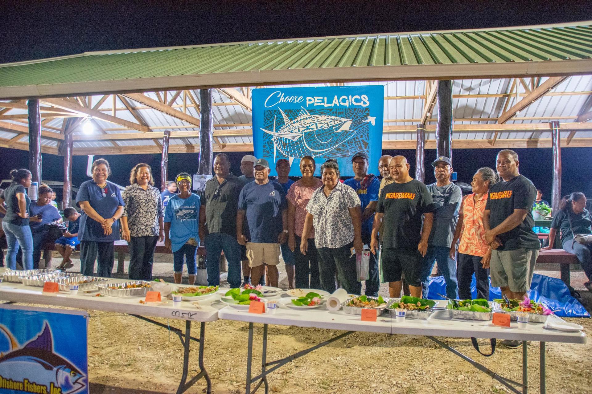 Group of people standing together under a pavilion, with a long table set with dishes.