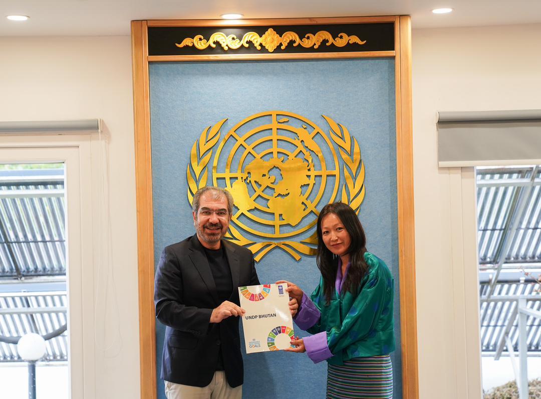Two people exchanging a document in front of a UN emblem backdrop.