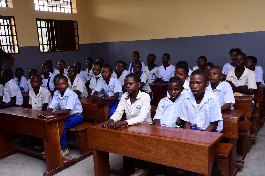 A classroom filled with students in white uniforms seated at wooden desks, attentively looking forward.
