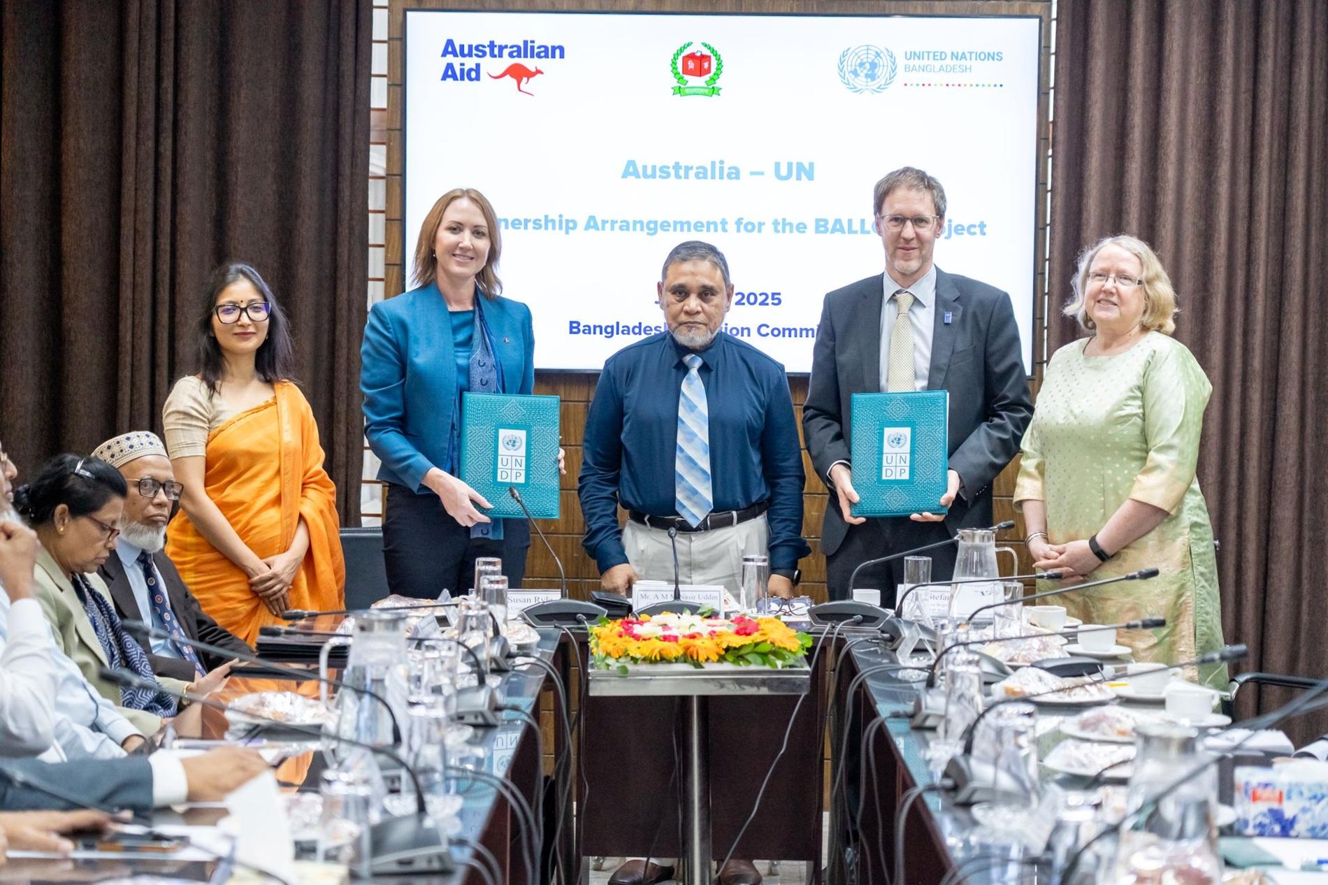 Six individuals stand around a table holding documents, smiling at a formal event.