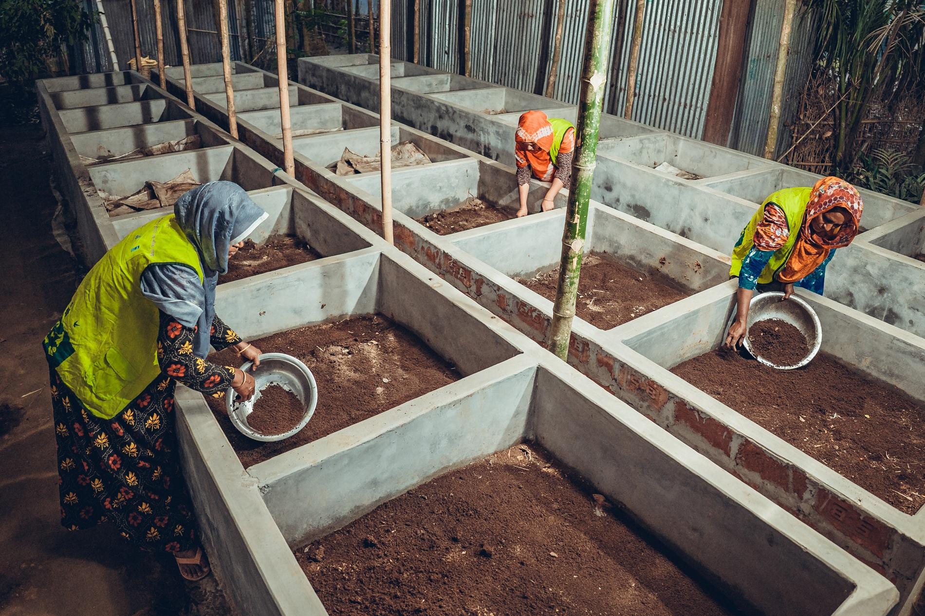 Two women in safety vests working in a garden box area, planting in soil.