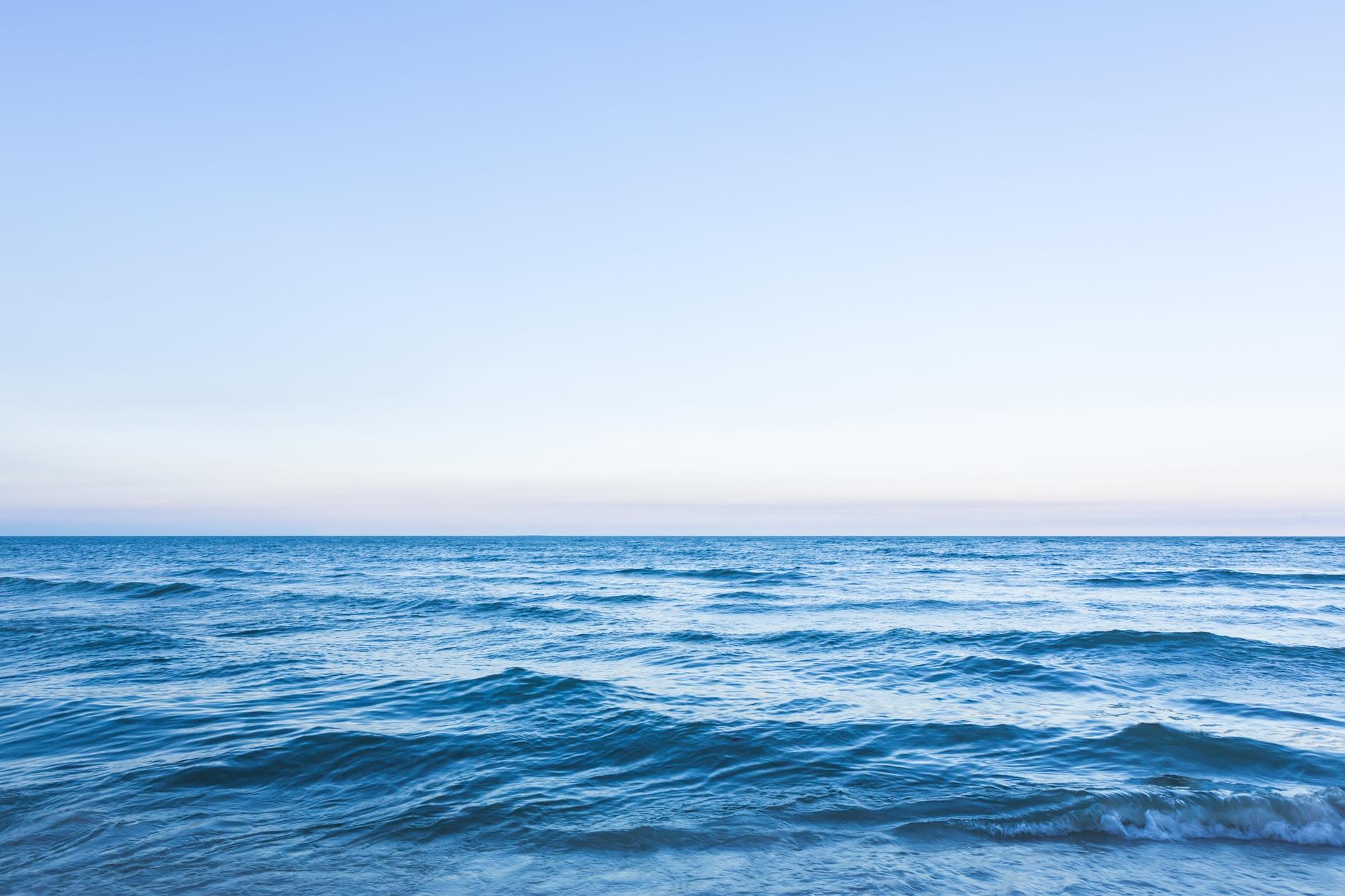 Calm ocean waves under a clear blue sky, stretching to the horizon.