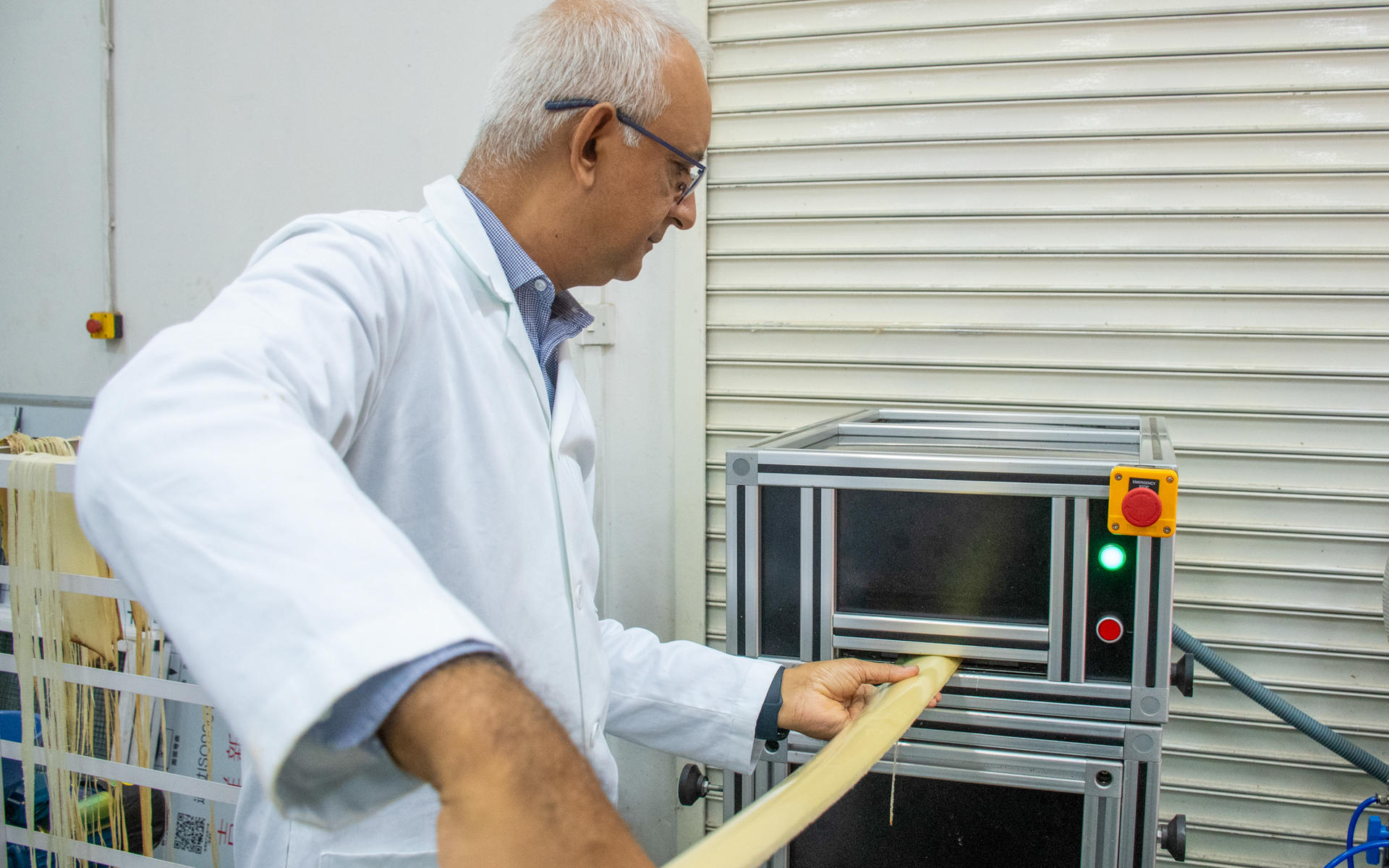 A man in a lab coat operates a machine, inserting a wooden strip into a device.