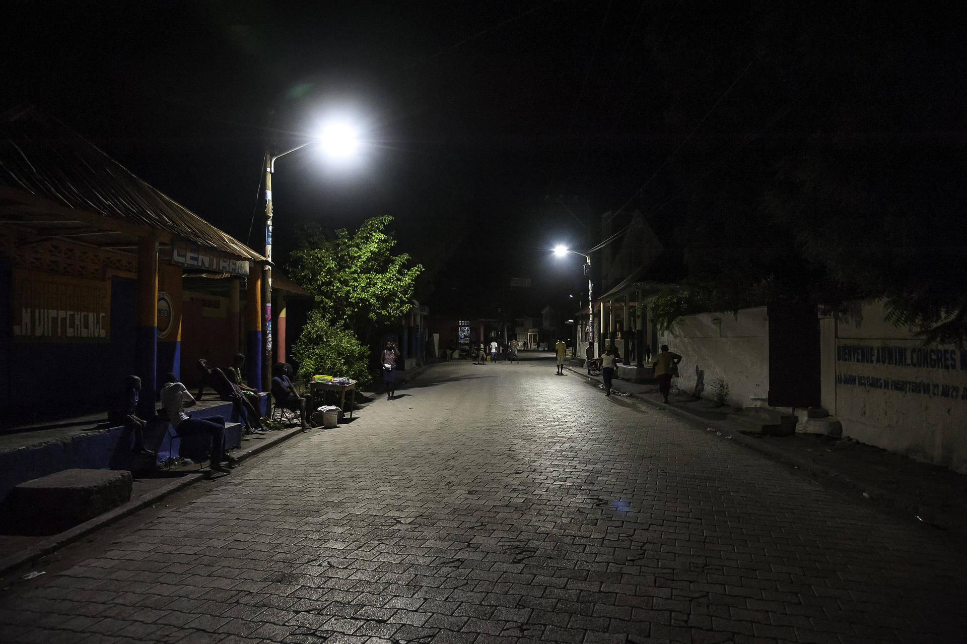 Quiet, dimly lit street at night with a few trees and buildings along the sides.