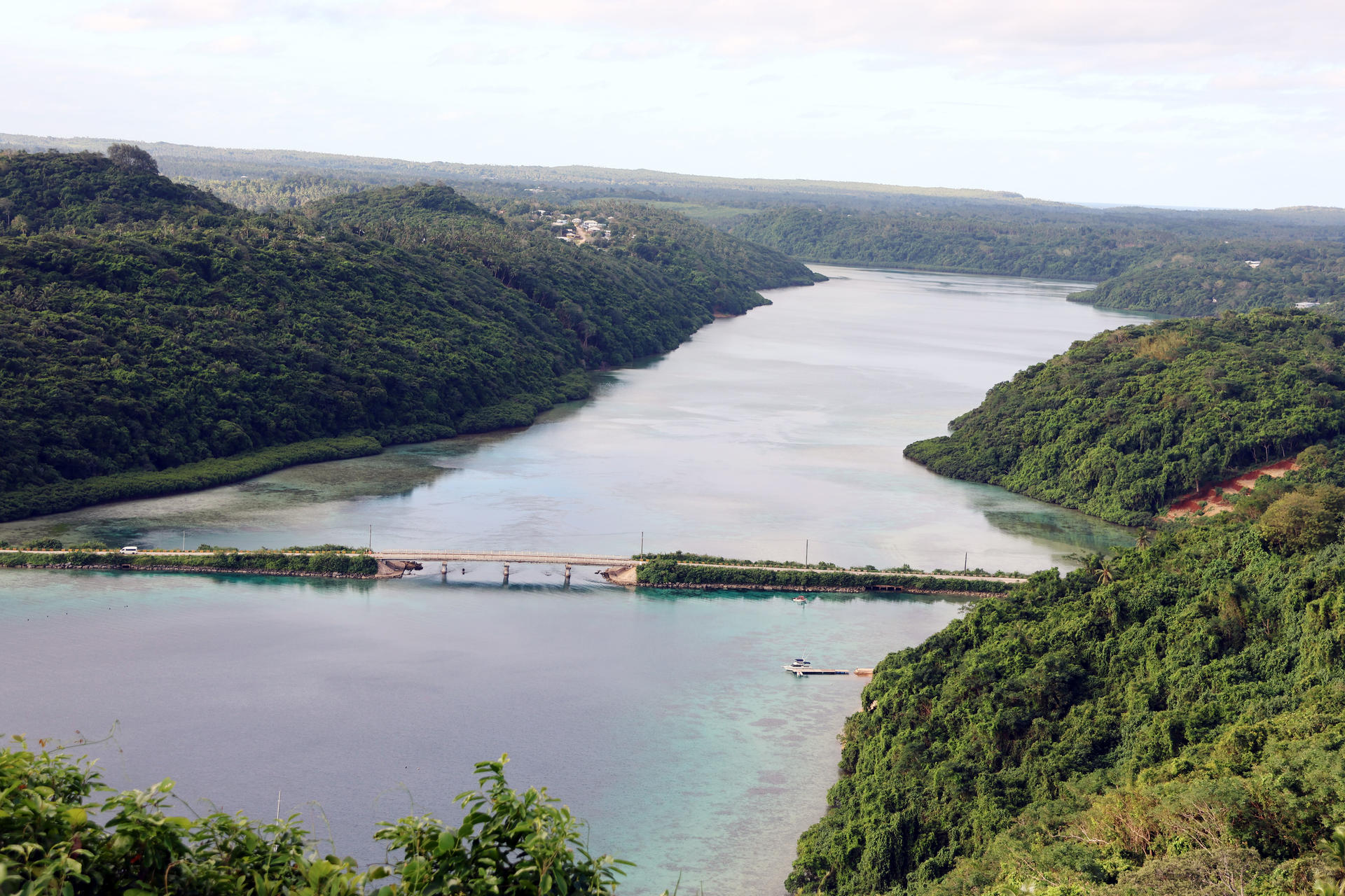 Lush green hills surround a winding river with a bridge spanning across it.