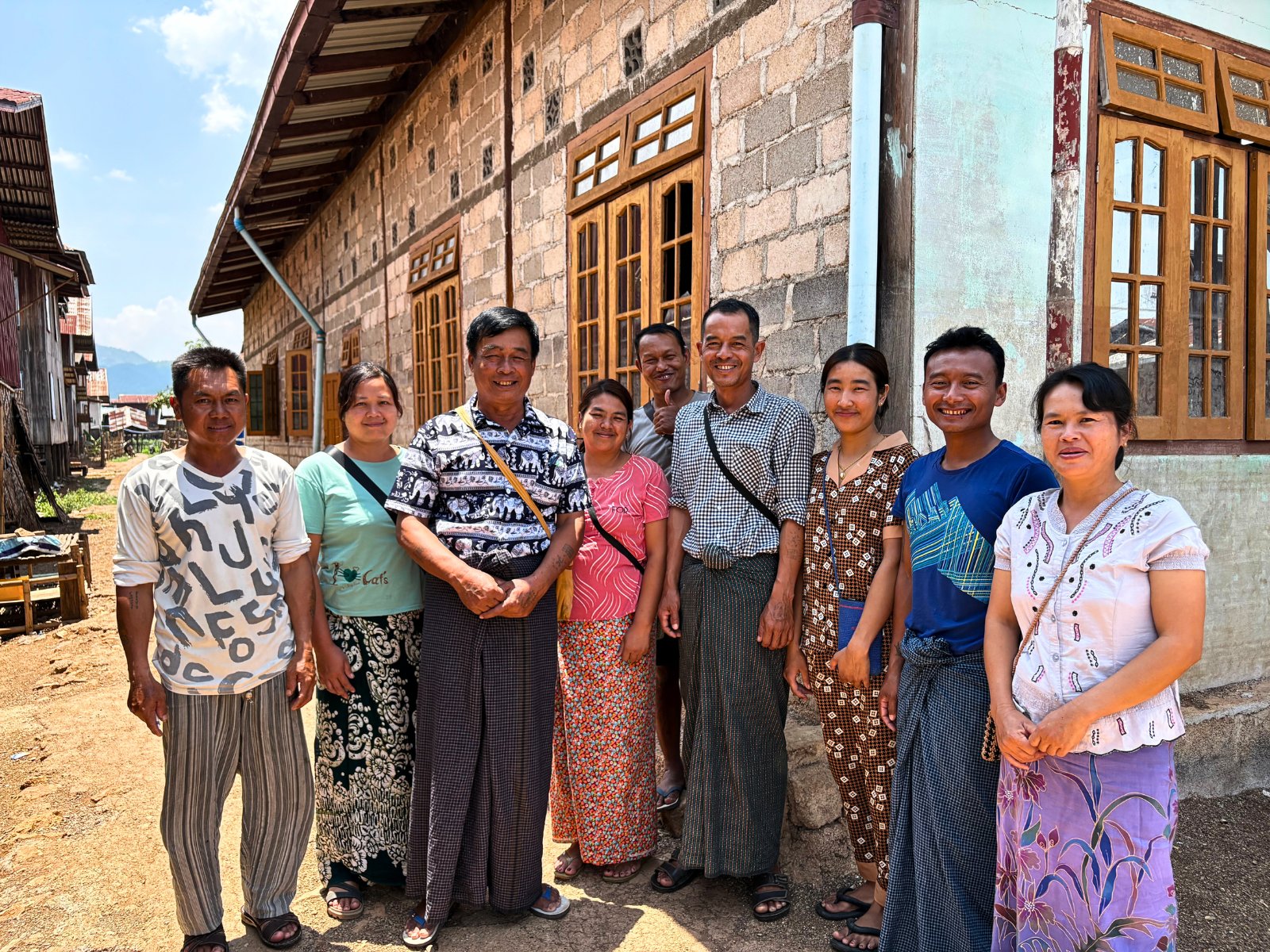 A group of ten men and women smiling together in front of a building with wooden windows.