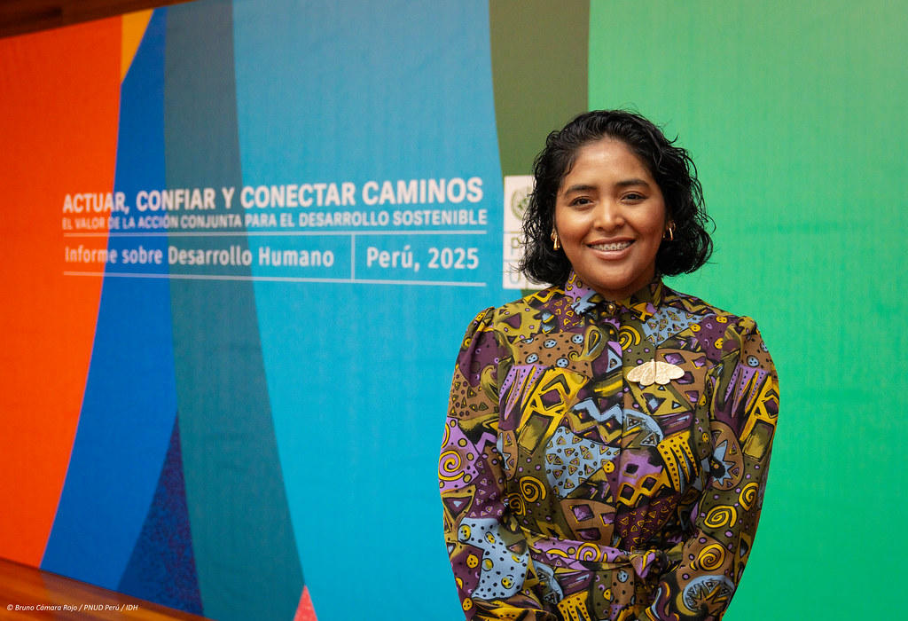 A woman smiles in front of a colorful backdrop featuring text about human development in Peru.
