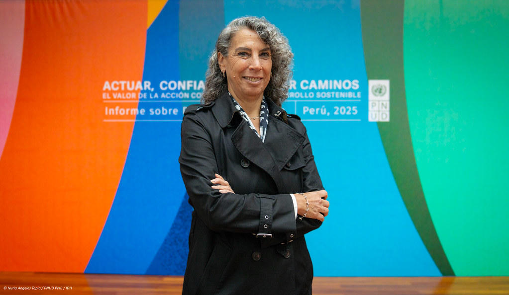 Woman in a black coat stands confidently with arms crossed against a colorful backdrop.