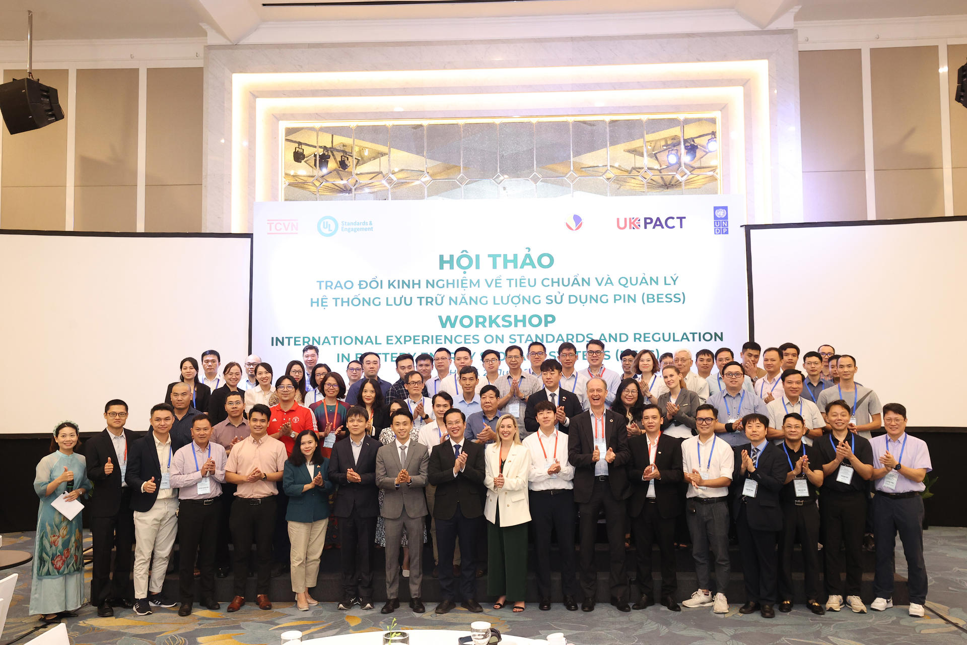 Group photo of participants at a workshop, smiling and applauding in a conference setting.