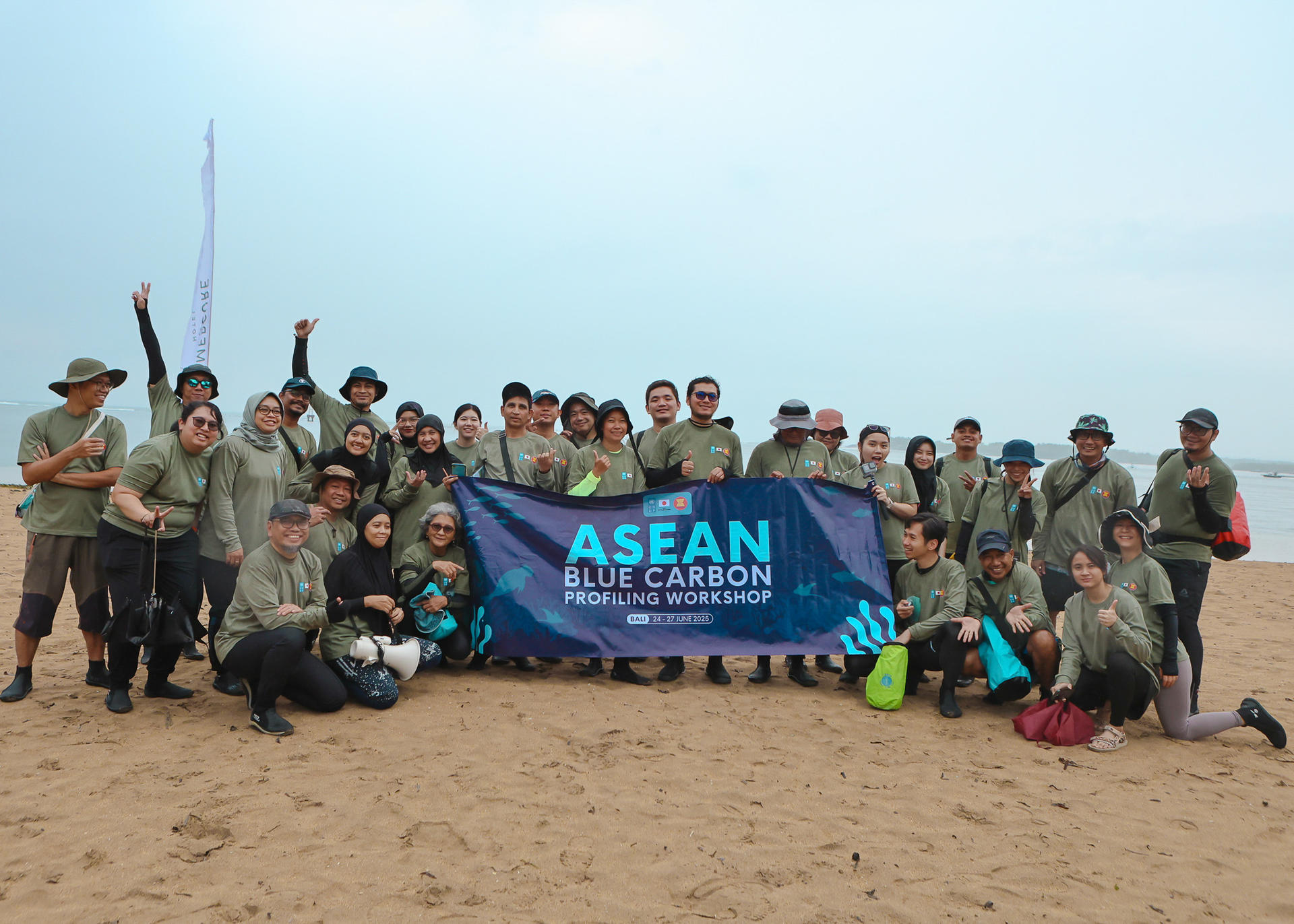 Group of people in matching shirts holding a banner on a sandy beach.