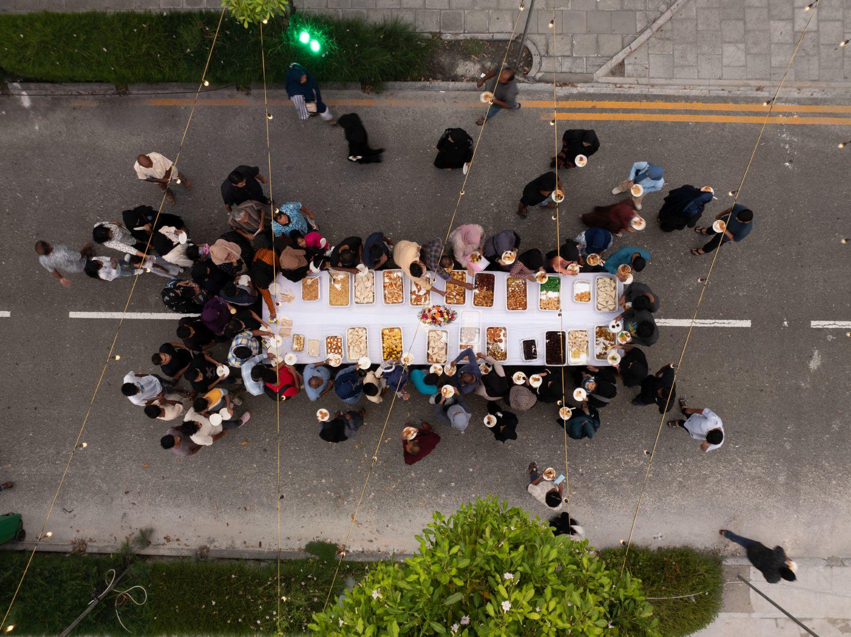 Aerial view of a long dining table set with food, surrounded by people on a street.