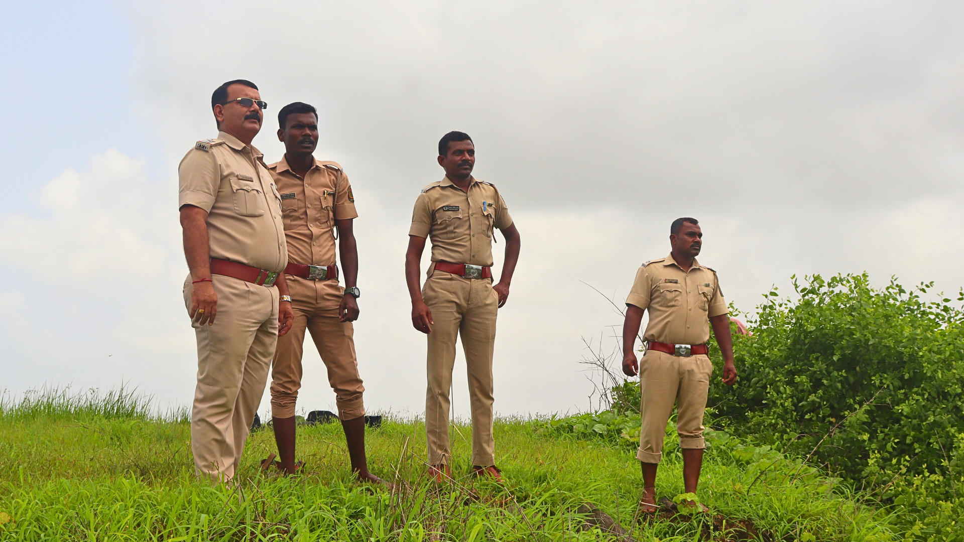 Four police officers in uniform standing on grass under a cloudy sky.