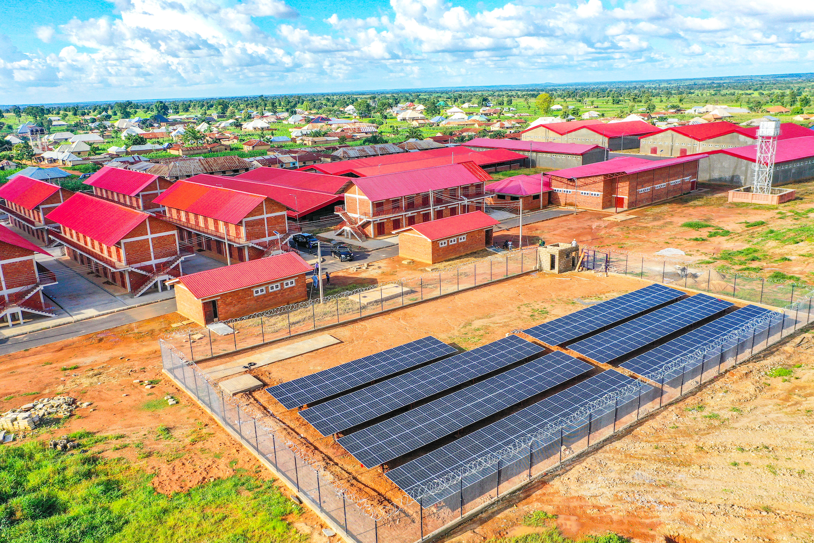 Aerial view of a facility with red-roofed buildings and solar panels in a dry landscape.